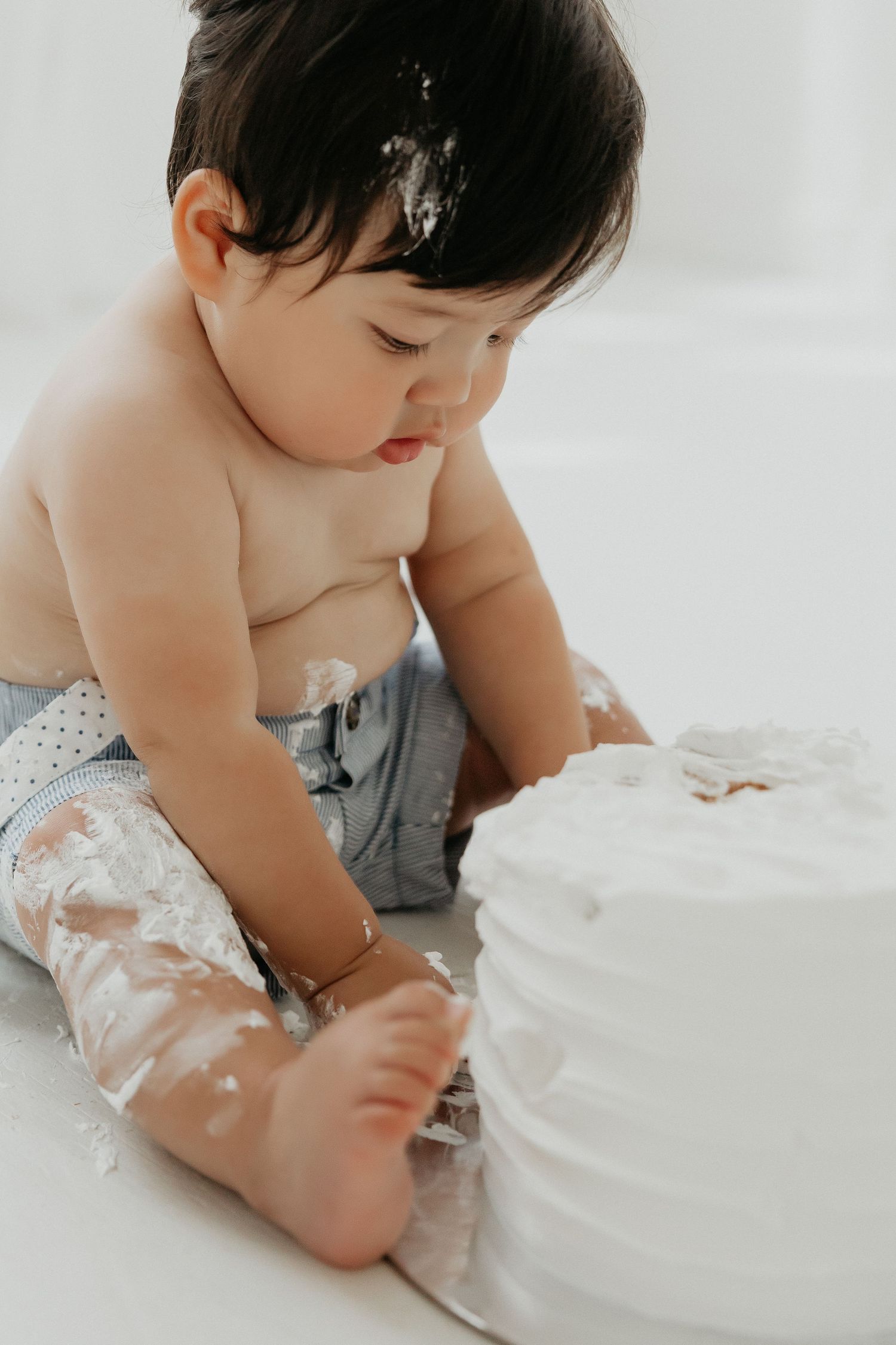 Baby plays with white frosted cake while wearing gray outfit.