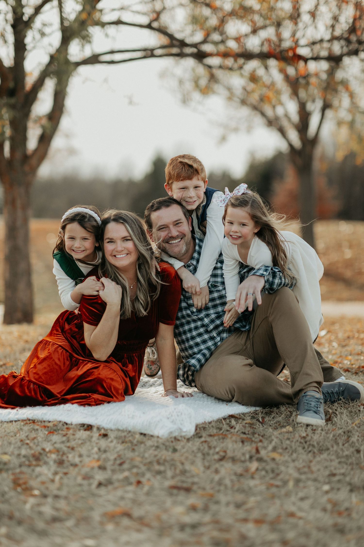 Family lying together on ground during autumn photoshoot with fallen leaves.