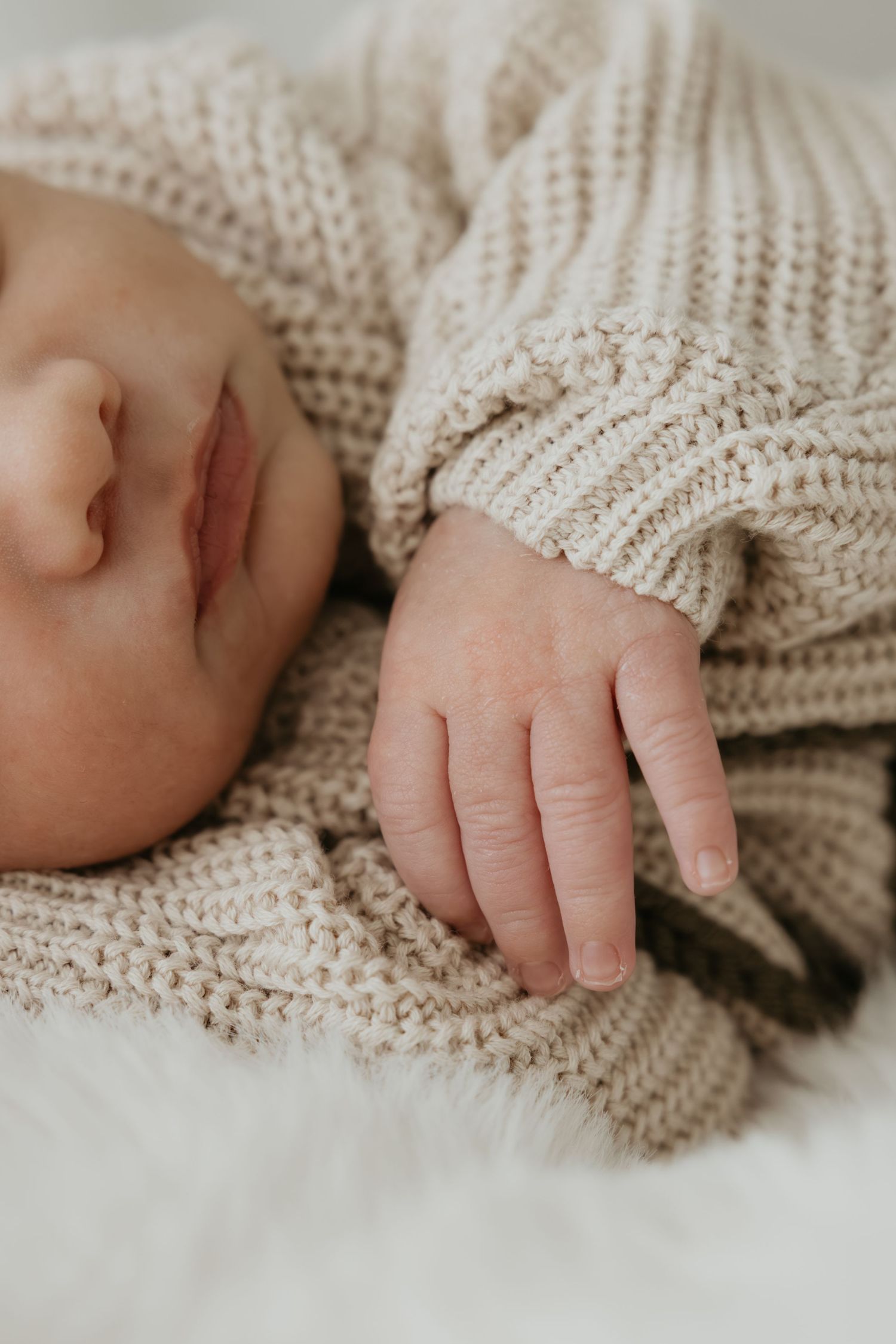 Delicate baby hands and fingers resting on cream knitted fabric.