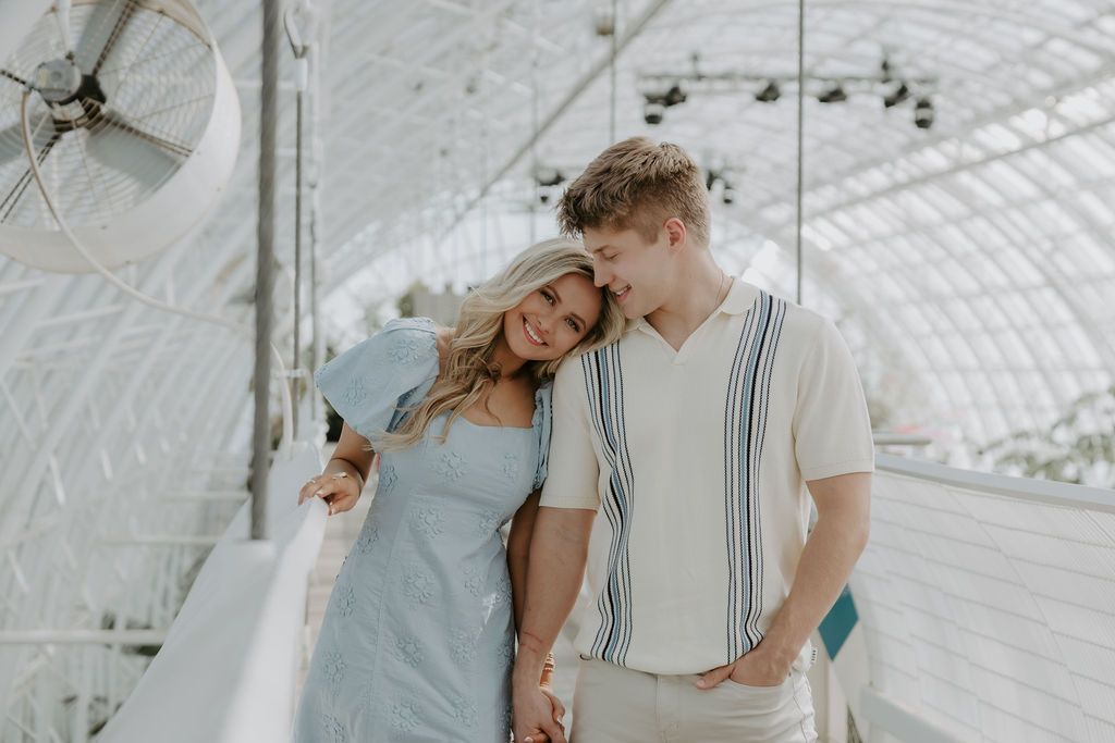 Romantic couple moments captured in bright greenhouse with white architectural details.