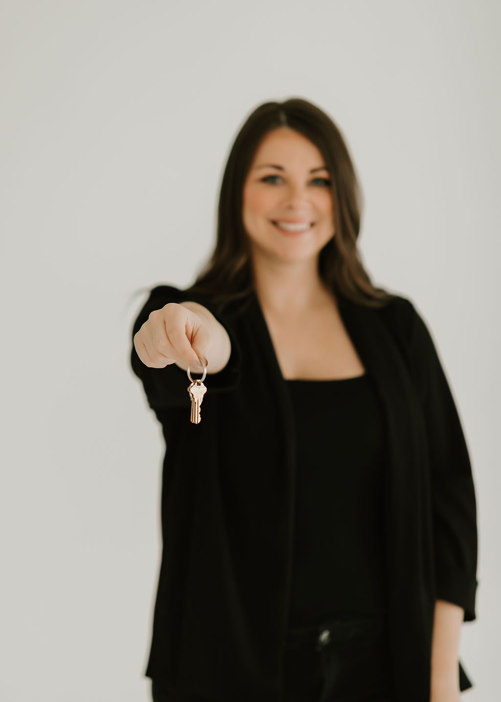 Professional portrait of someone in black blazer holding up keys against white background.
