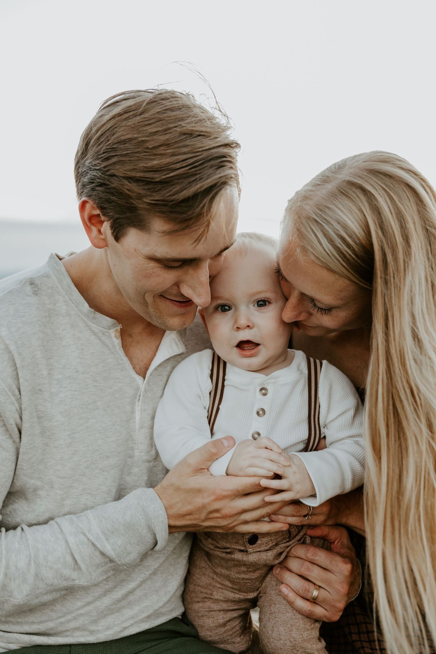 A loving family shares tender moments together in matching grey outfits against a white background.