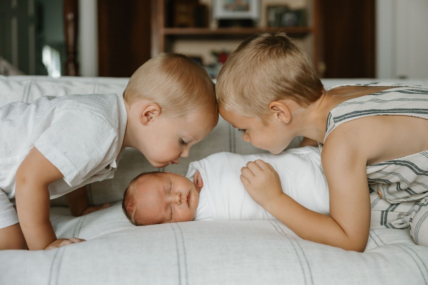 Sweet moment of siblings lying close together on white bedding.