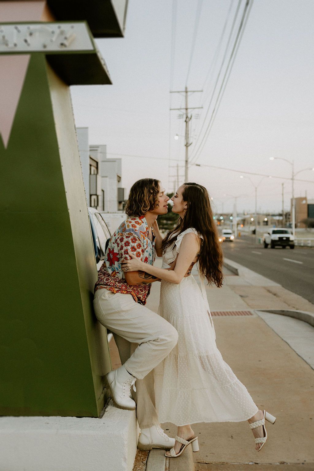 A couple embraces playfully outside a retro-styled building.