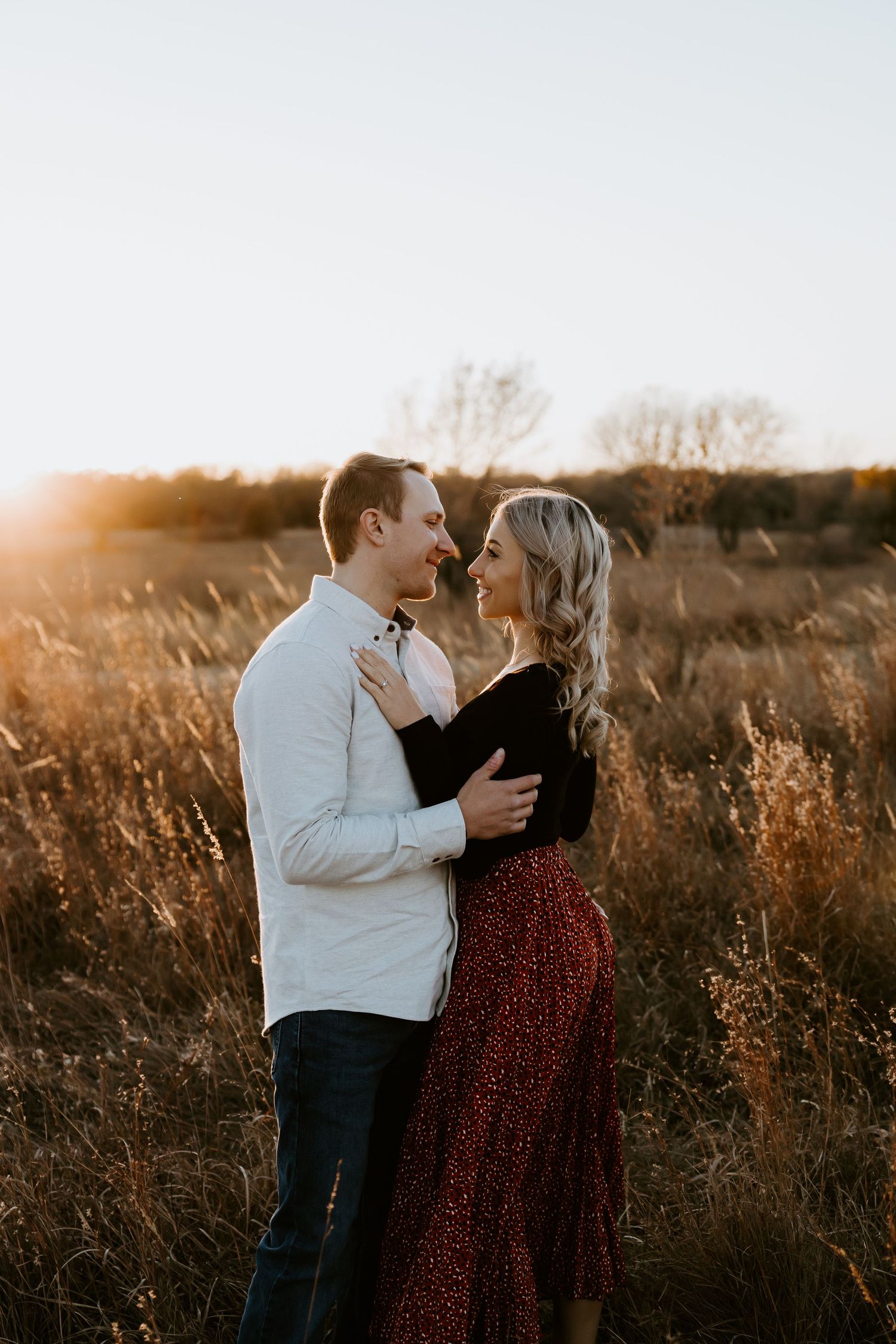 Romantic couple laughing together in a sunlit field at golden hour.