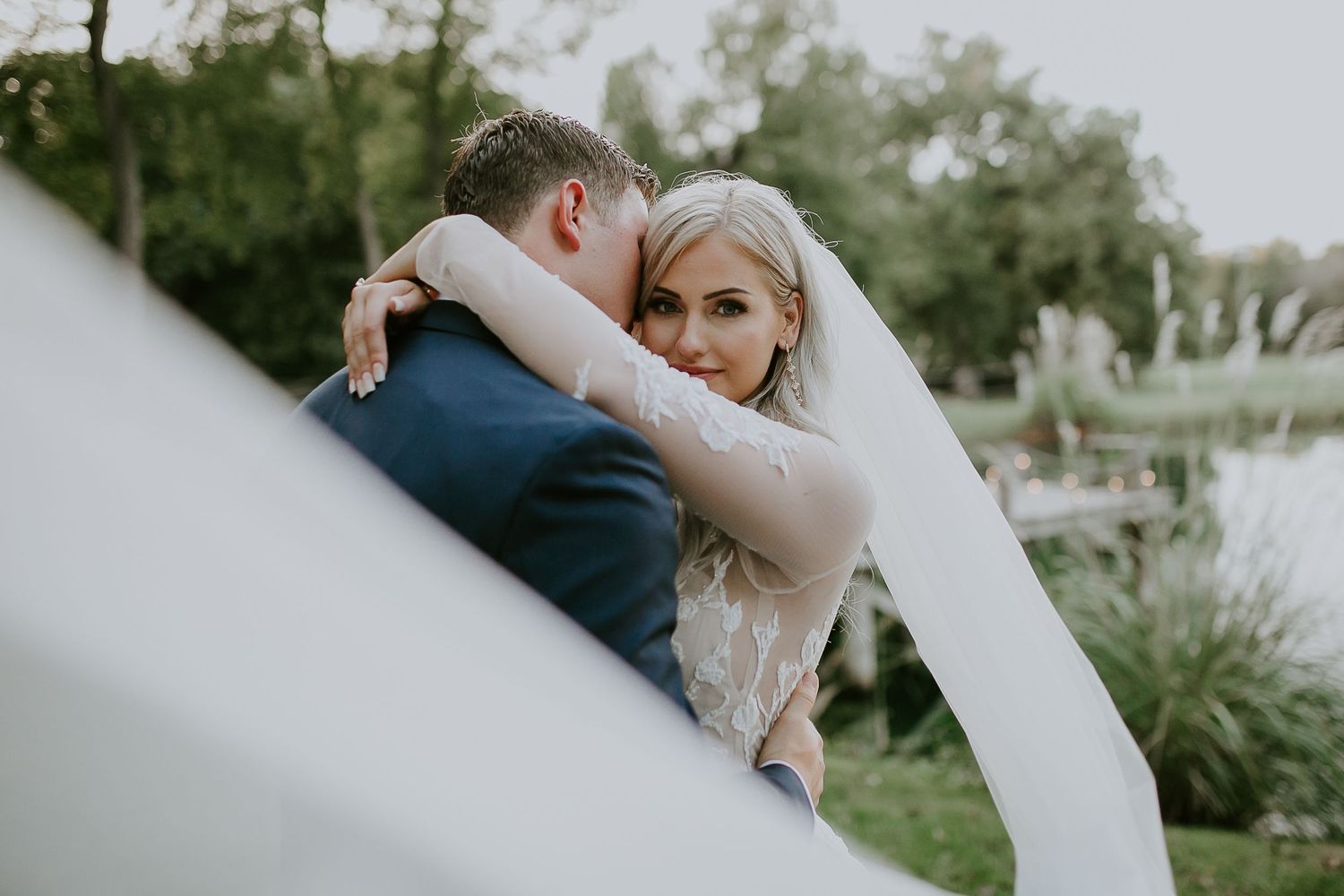 A romantic outdoor wedding scene with a flowing white veil and greenery in the background.