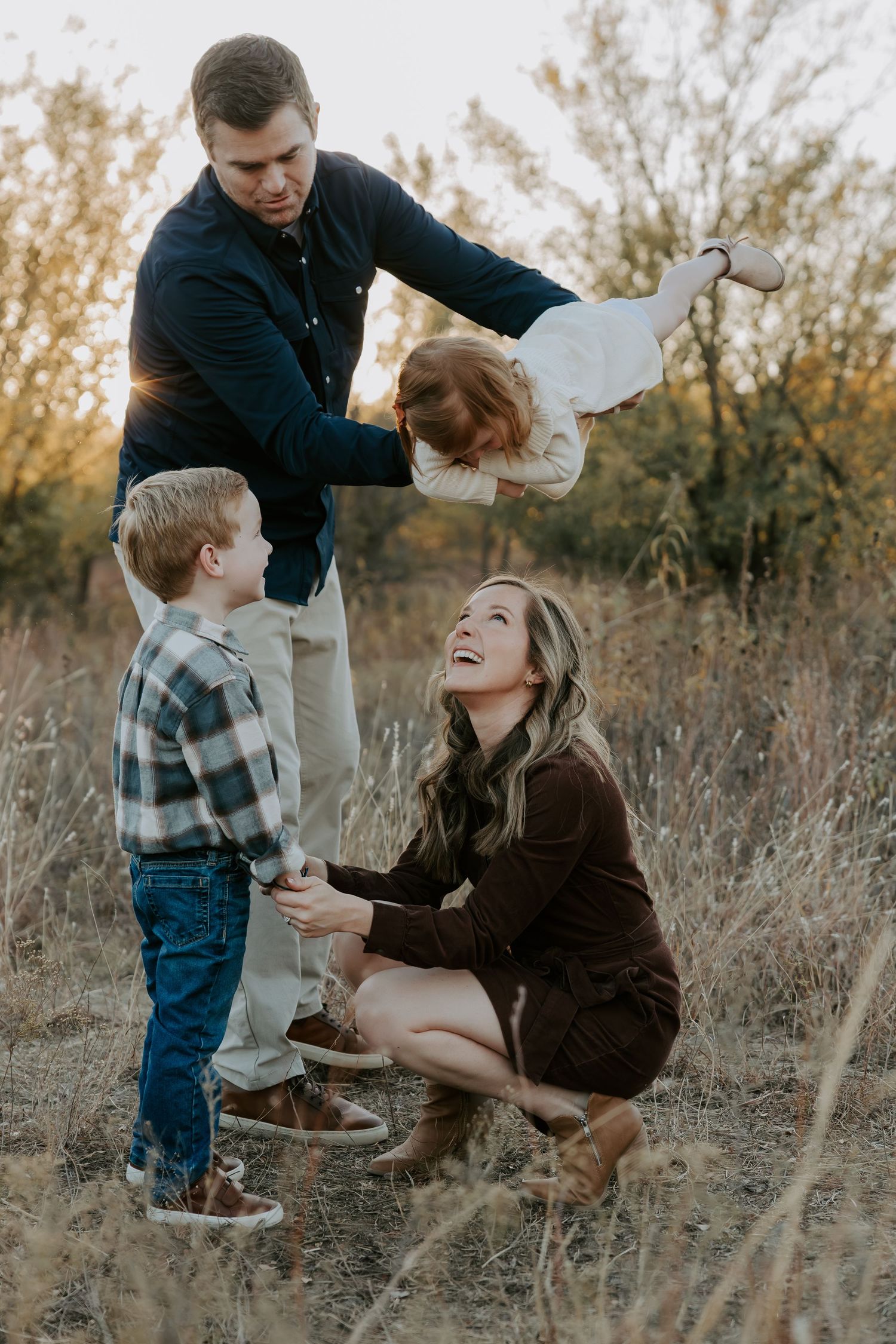 A family playing together in tall autumn grass during golden hour.