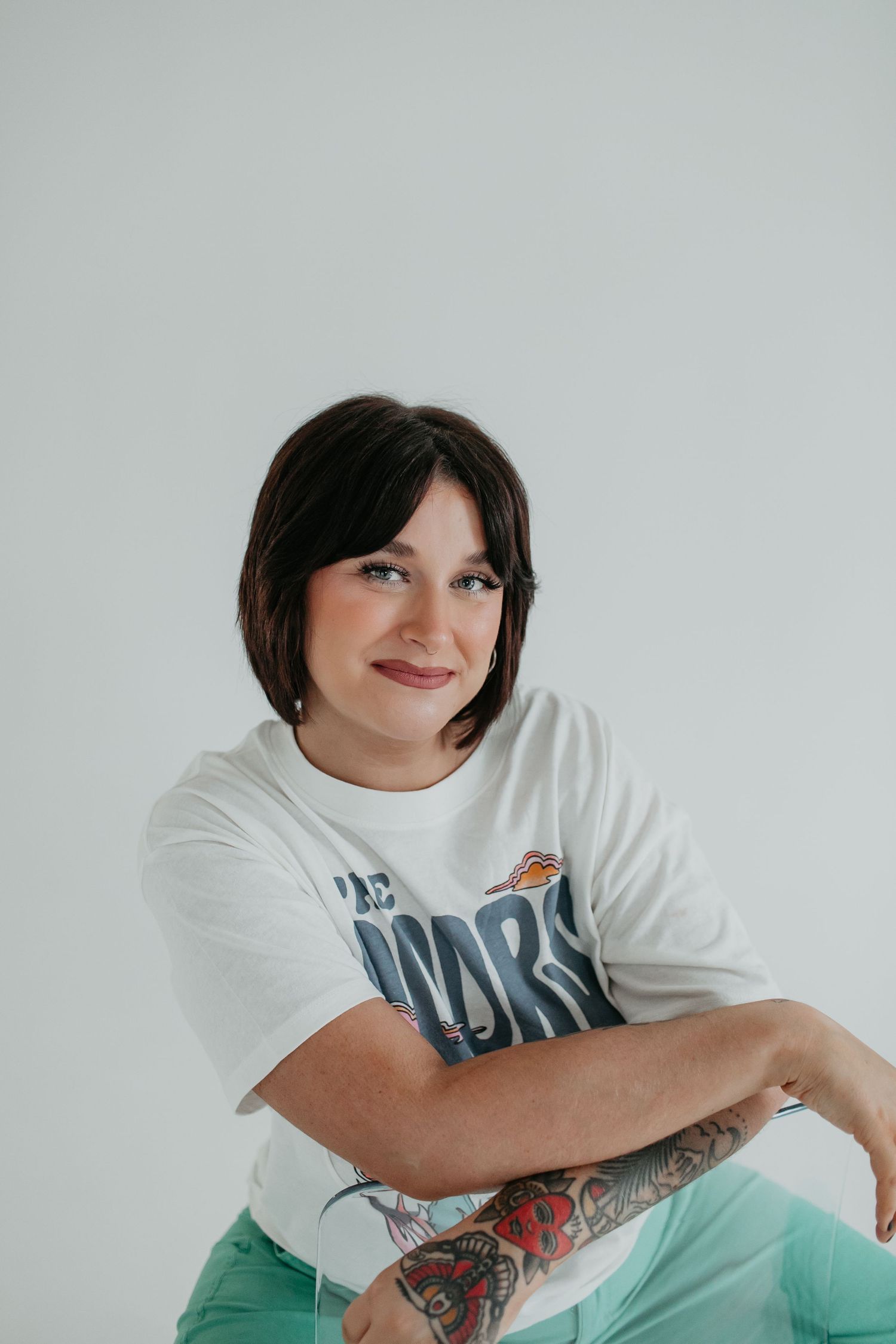 Casual portrait with tattoo wearing white graphic t-shirt against light background.