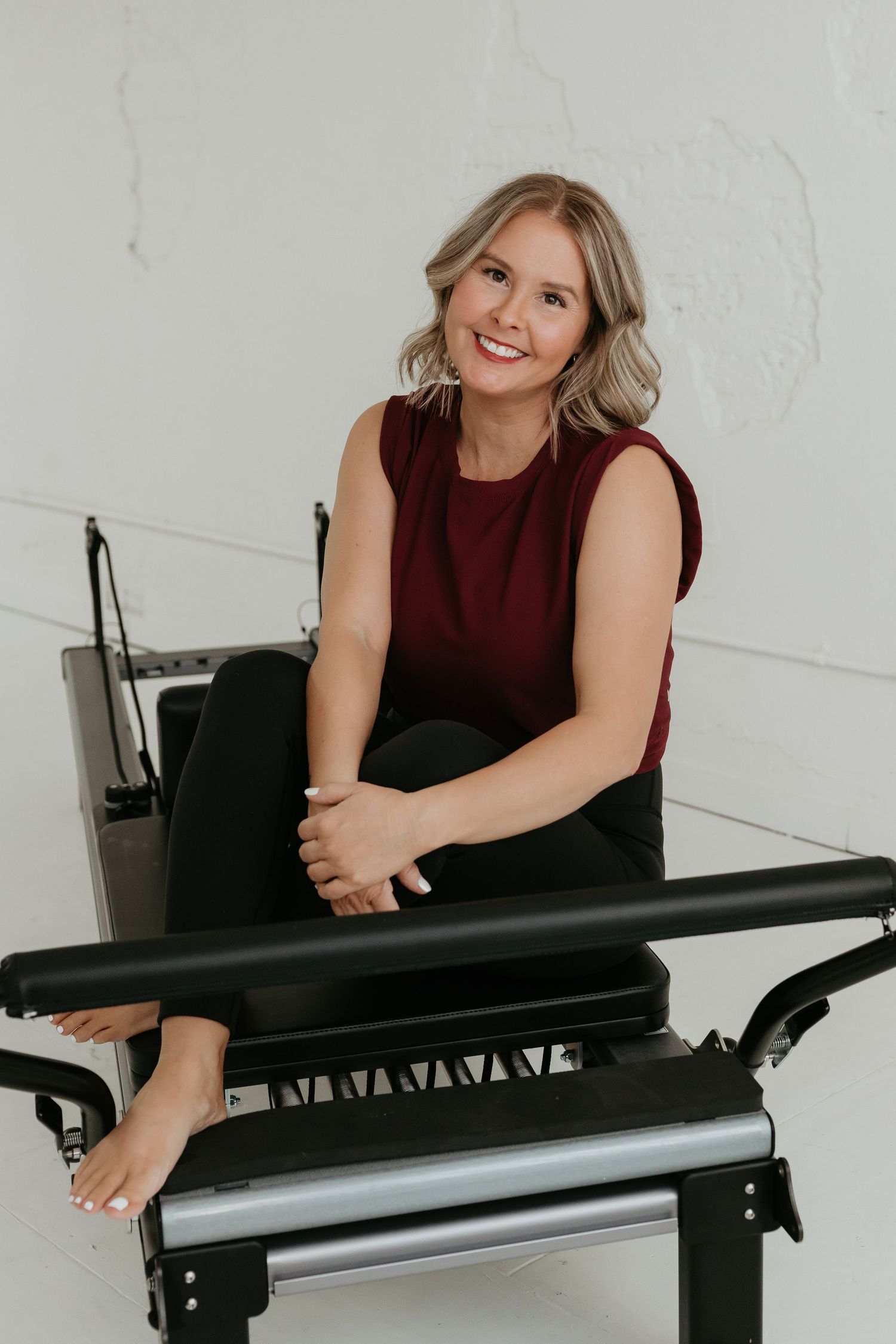 Person in burgundy top sitting casually on black furniture in studio setting.
