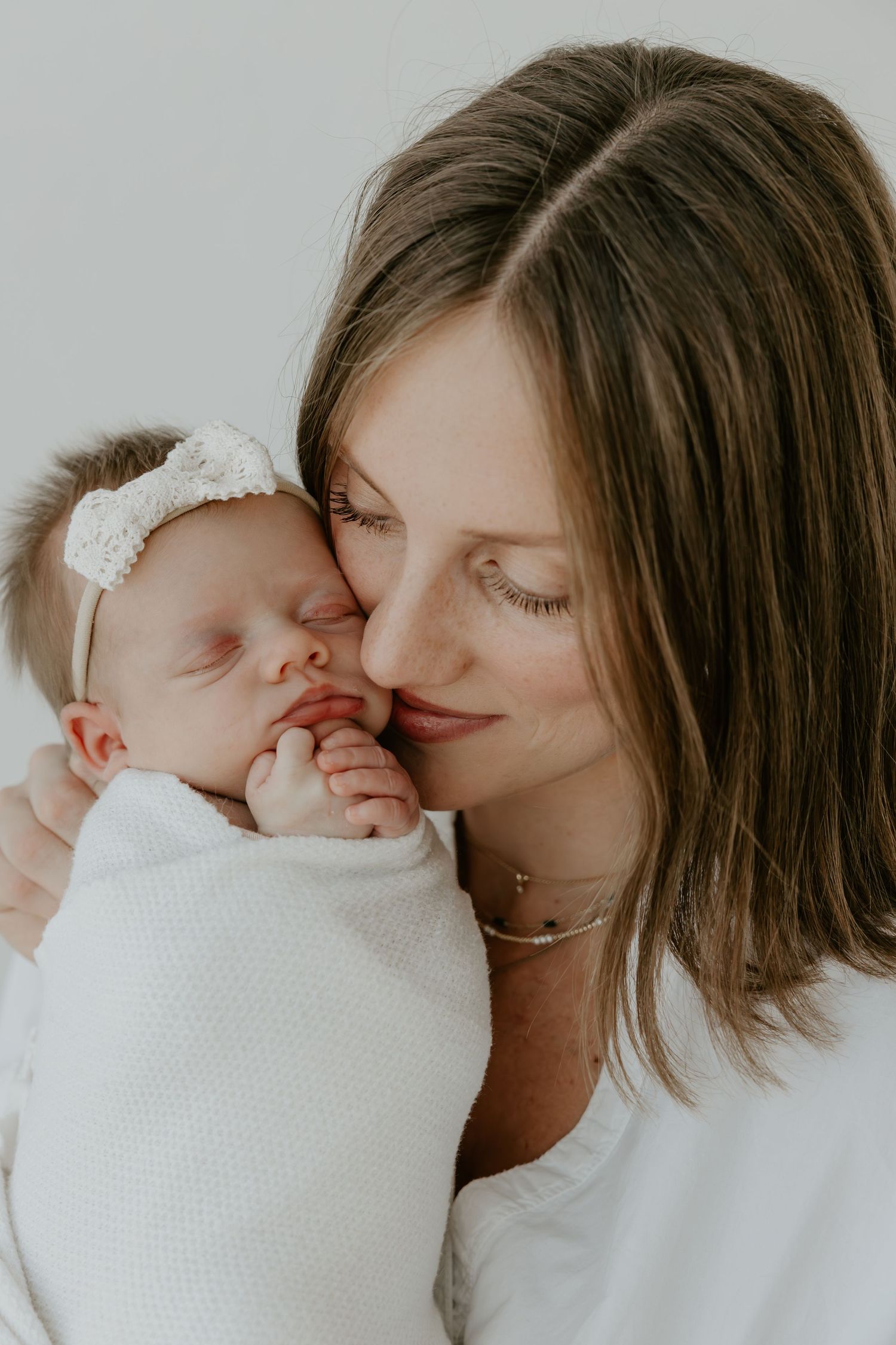 A tender moment captured in soft lighting as a parent gently kisses their newborn wrapped in white.