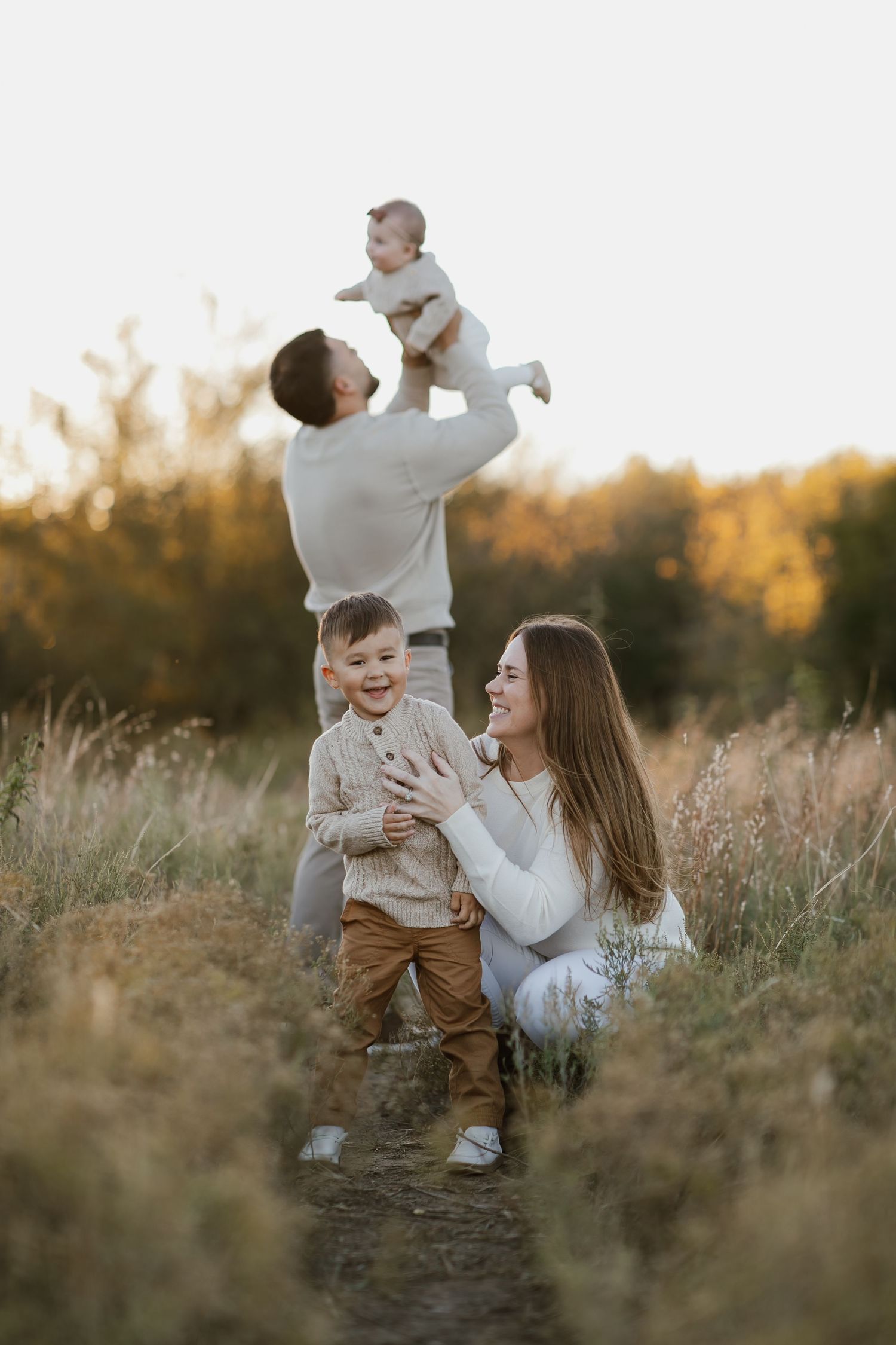 Playful family interactions in a sun-lit field with tall grass during golden hour.