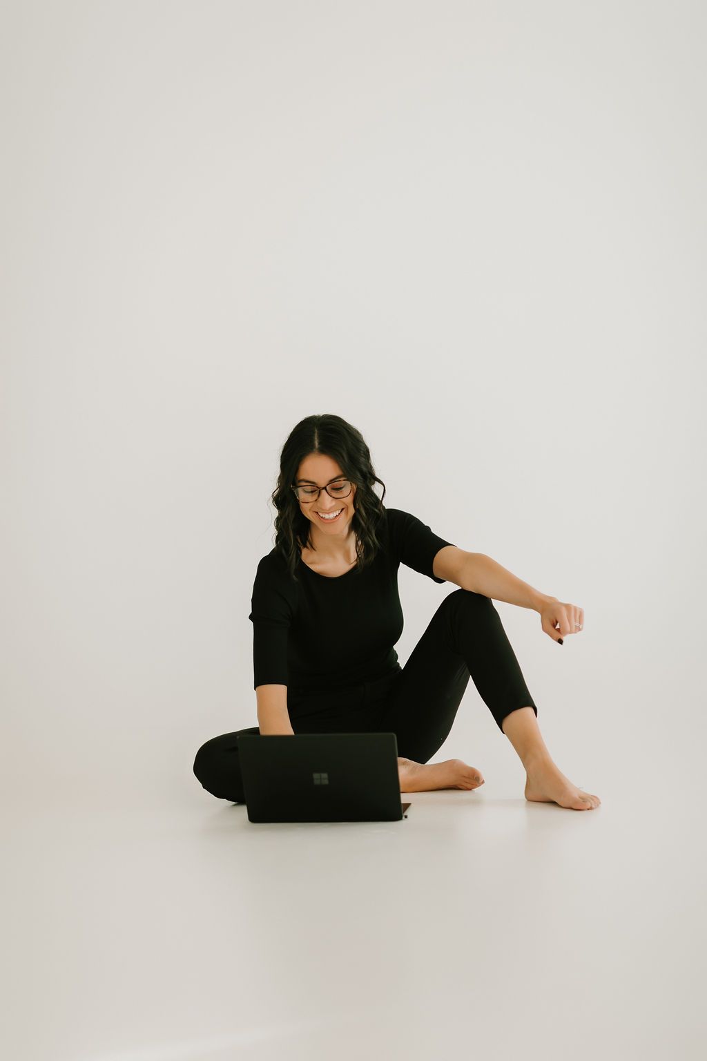 Casual portrait of someone working on laptop while sitting on floor in black outfit.