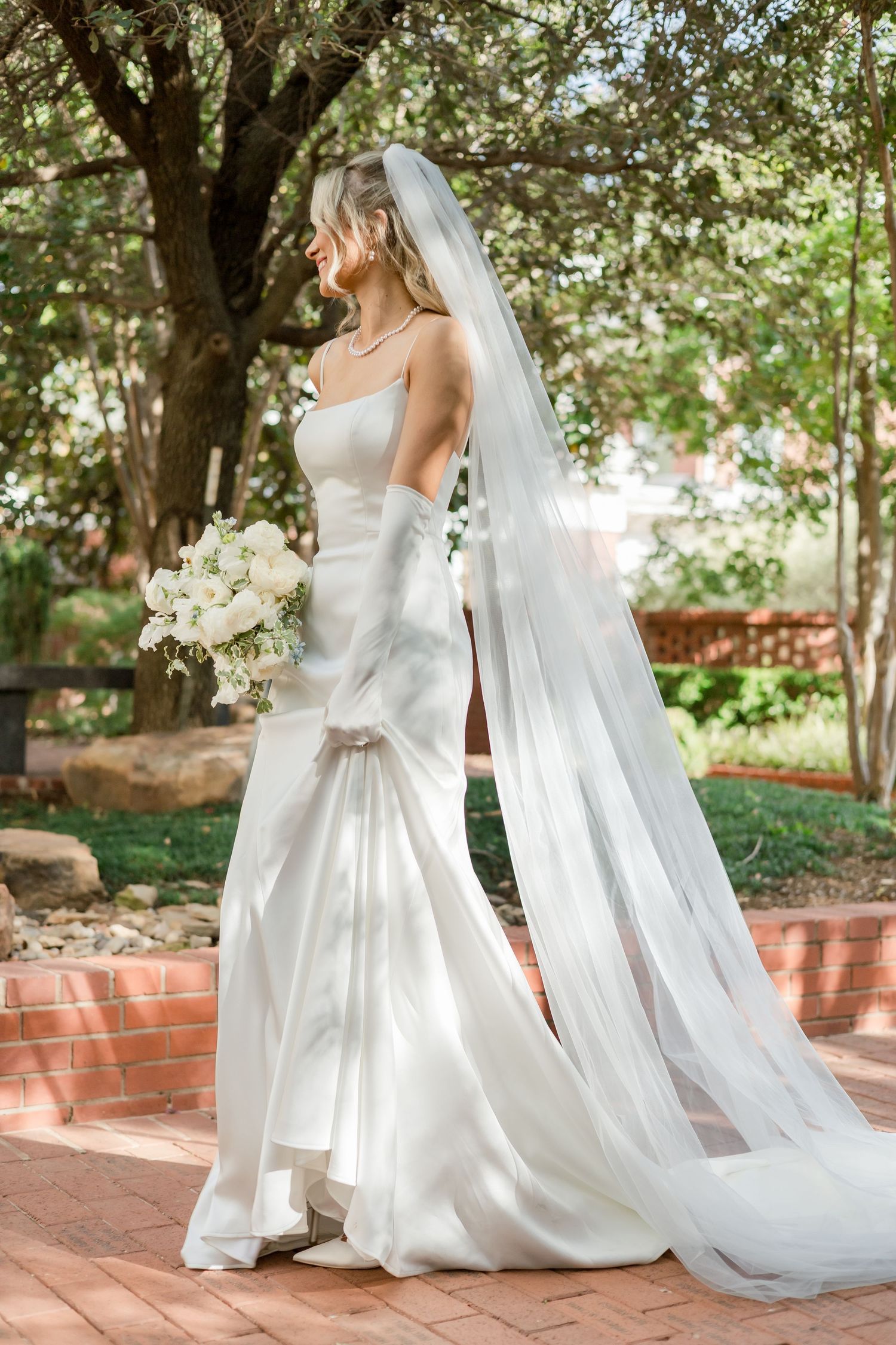 Elegant bridal portraits showing flowing white dress and veil on brick pathway.