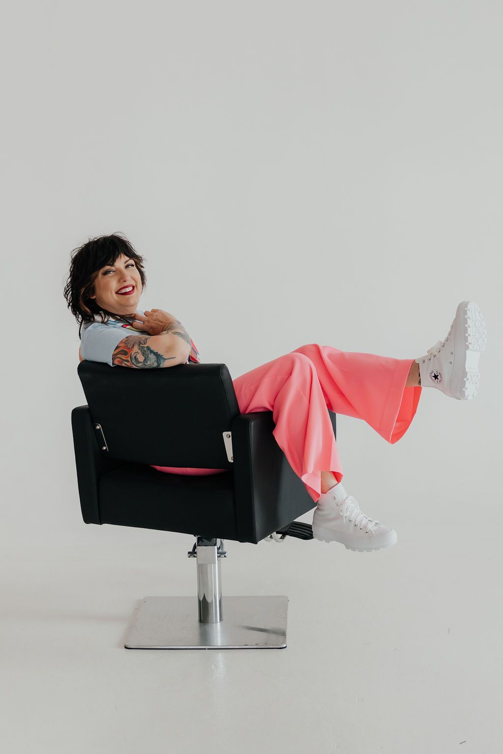 Playful studio shot of someone lounging sideways in modern black chair wearing pink pants.