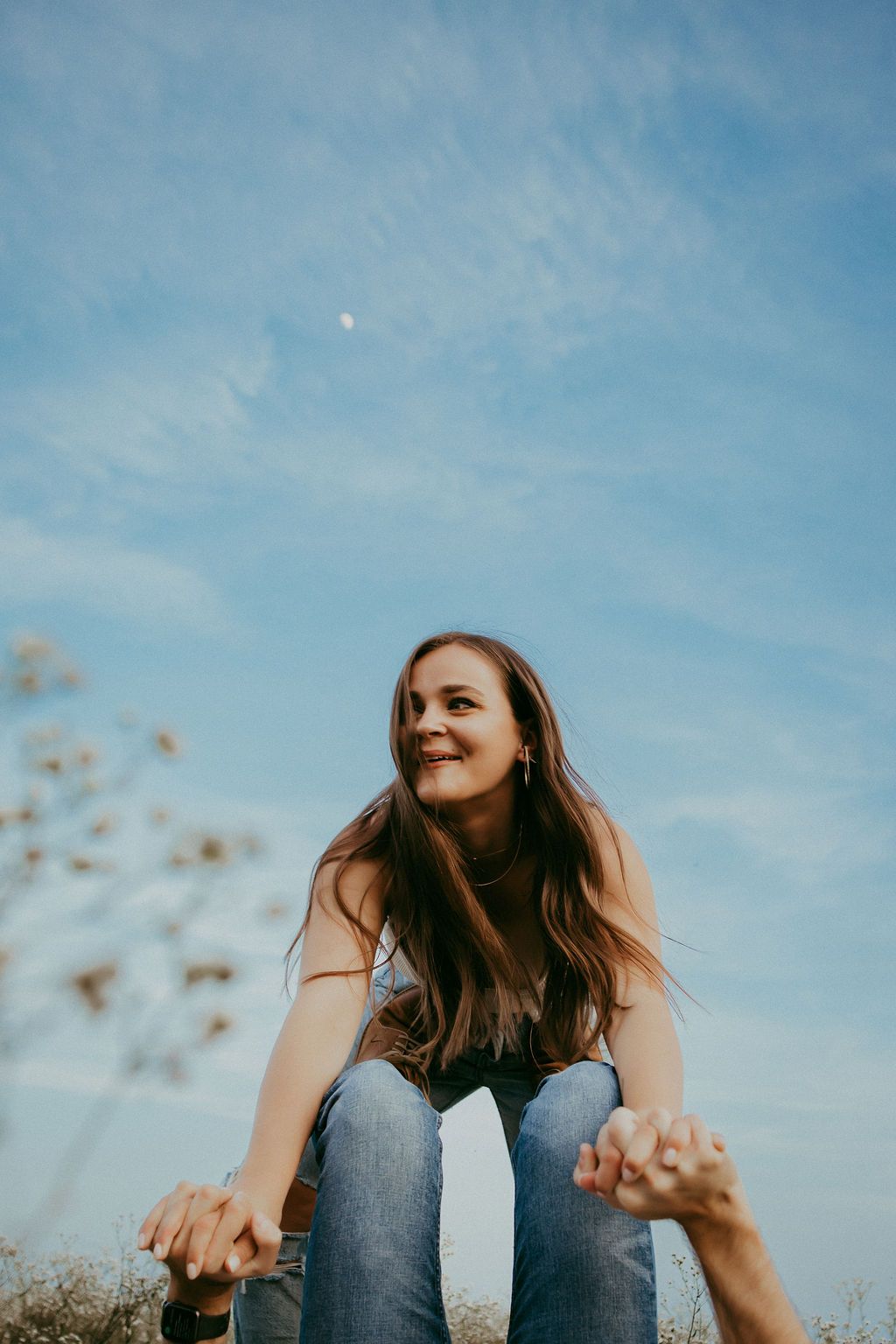 Person sitting outdoors with joyful expressions against blue sky background.