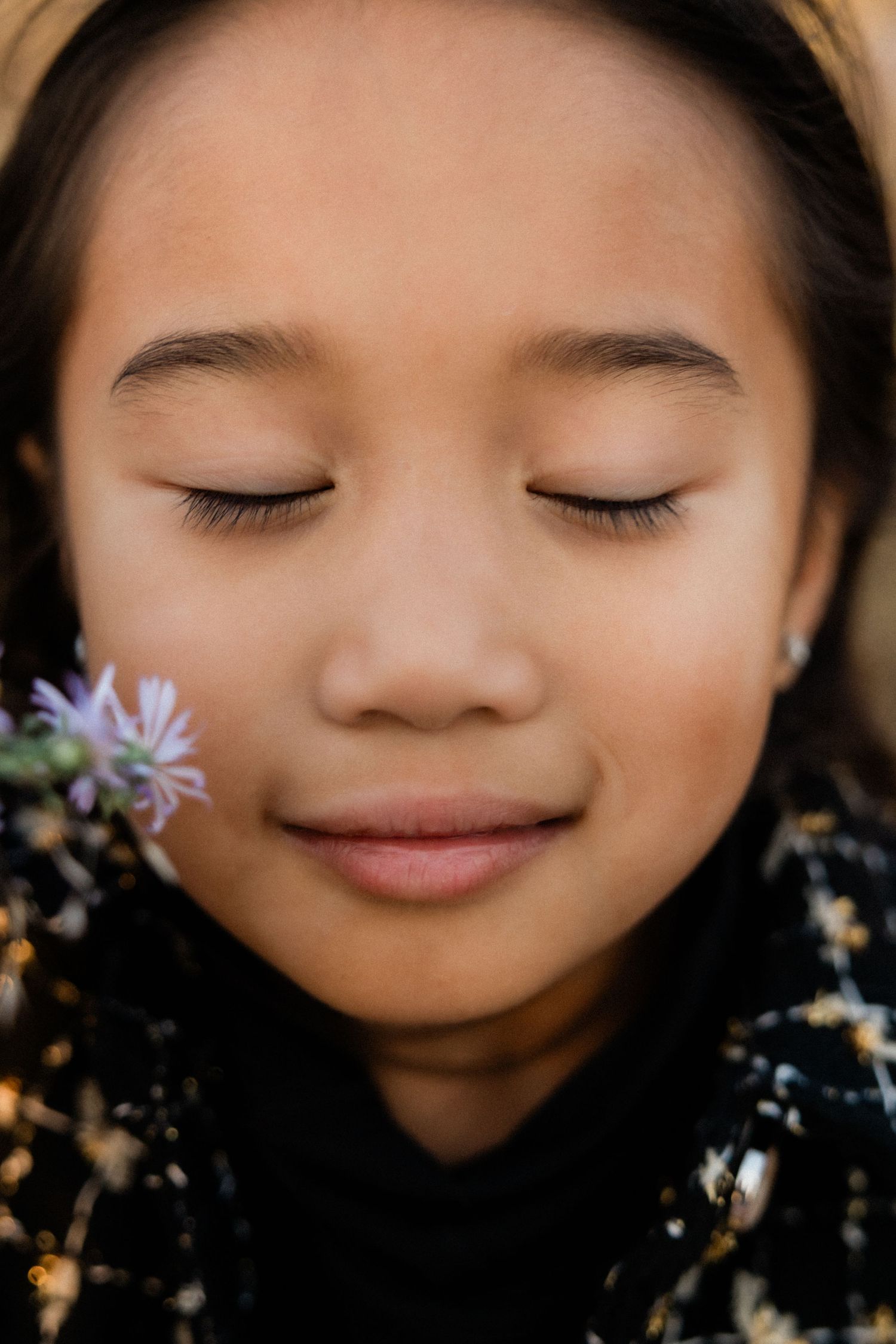 Close up portrait series showing a gentle smile and closed eyes with purple flowers in soft focus.