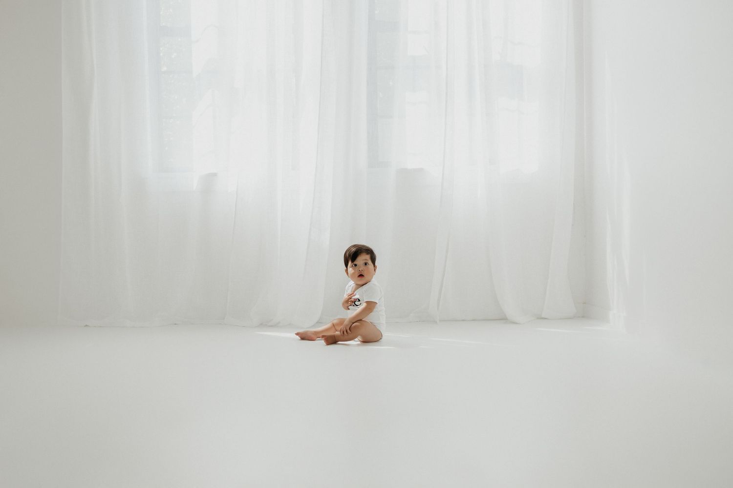 Baby in white and gray outfit sits against bright white backdrop.