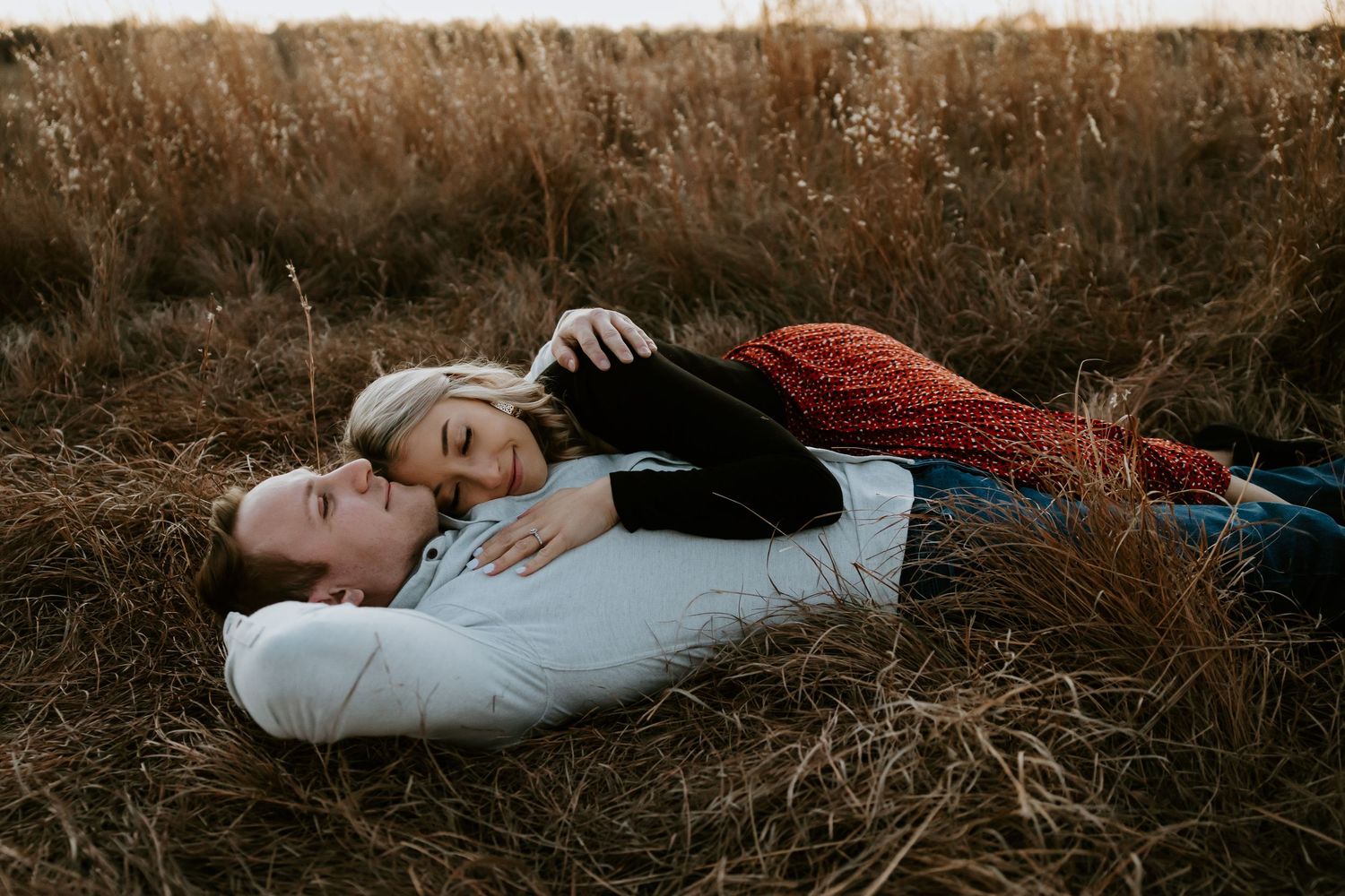 Couple lying in tall grass during an intimate outdoor photo session.