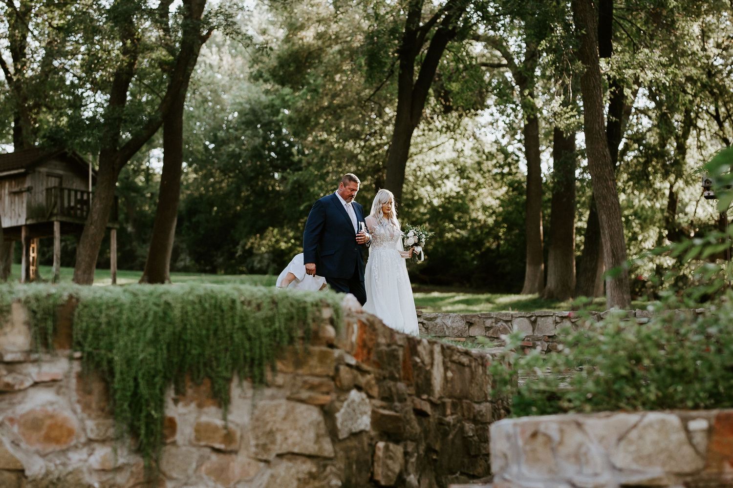 Wedding couple embracing in a romantic garden setting with stone walls and trees.