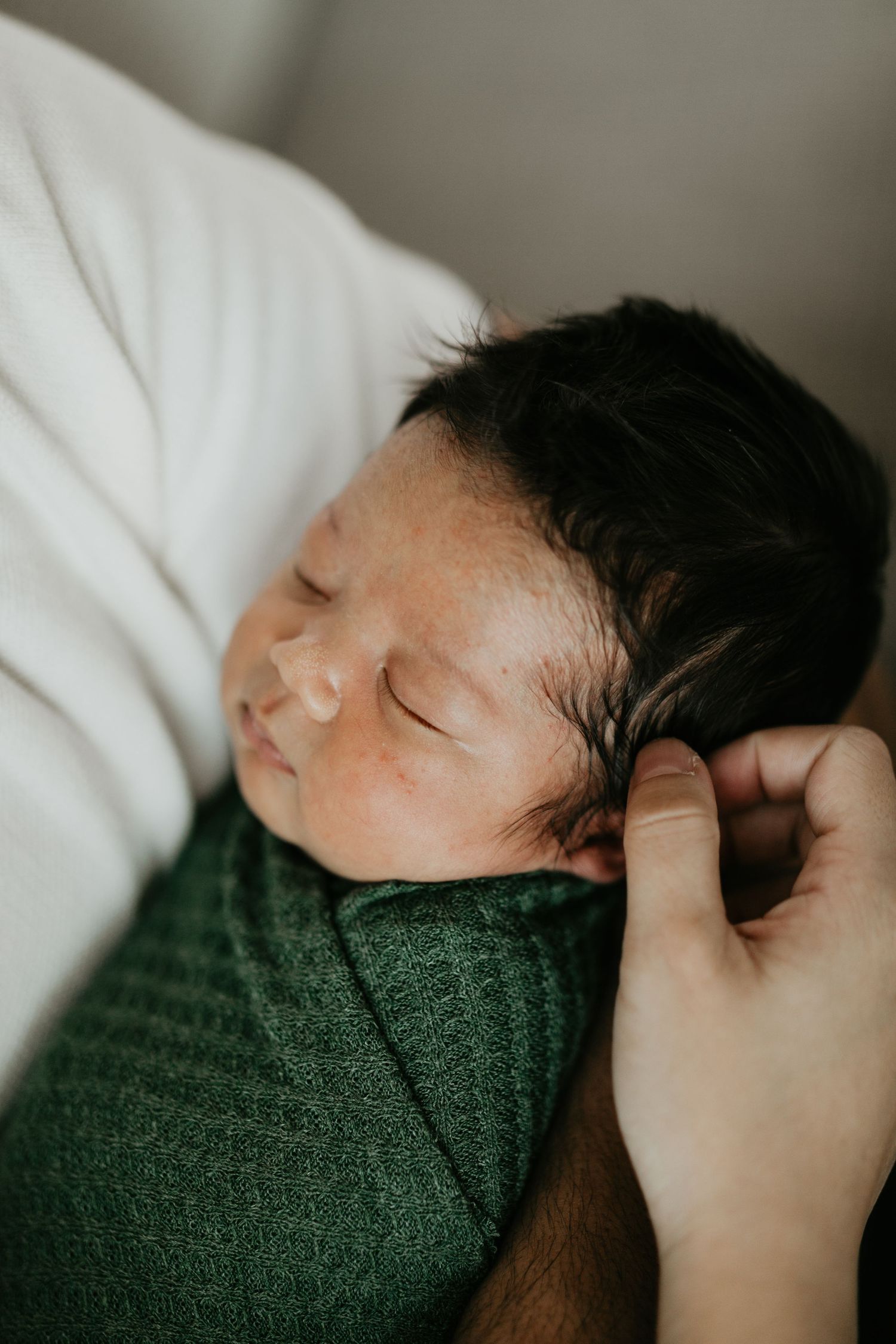Sleeping newborn wrapped in dark green blanket during intimate photo session.