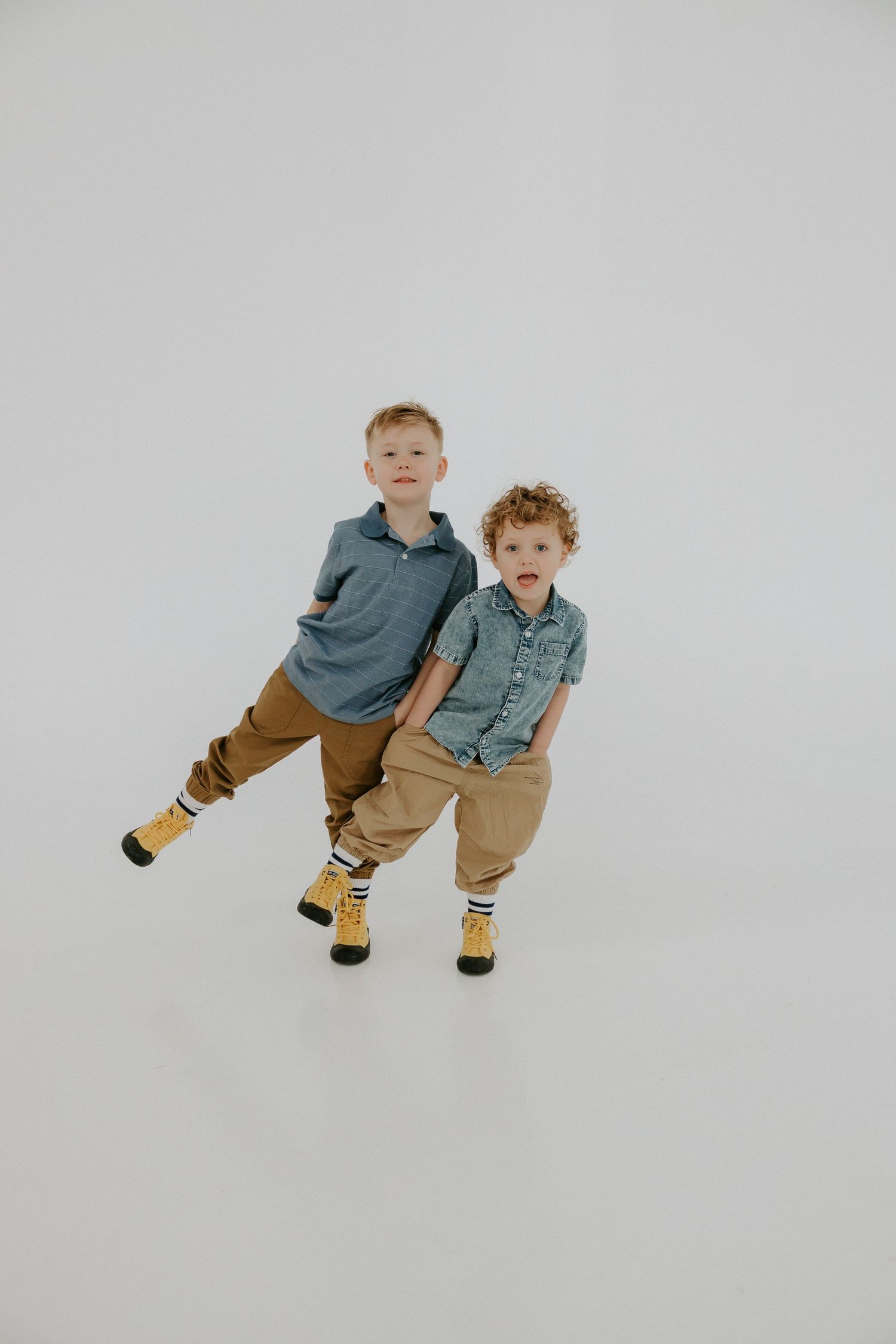 Two children in casual clothing playing and posing together against white backdrop.