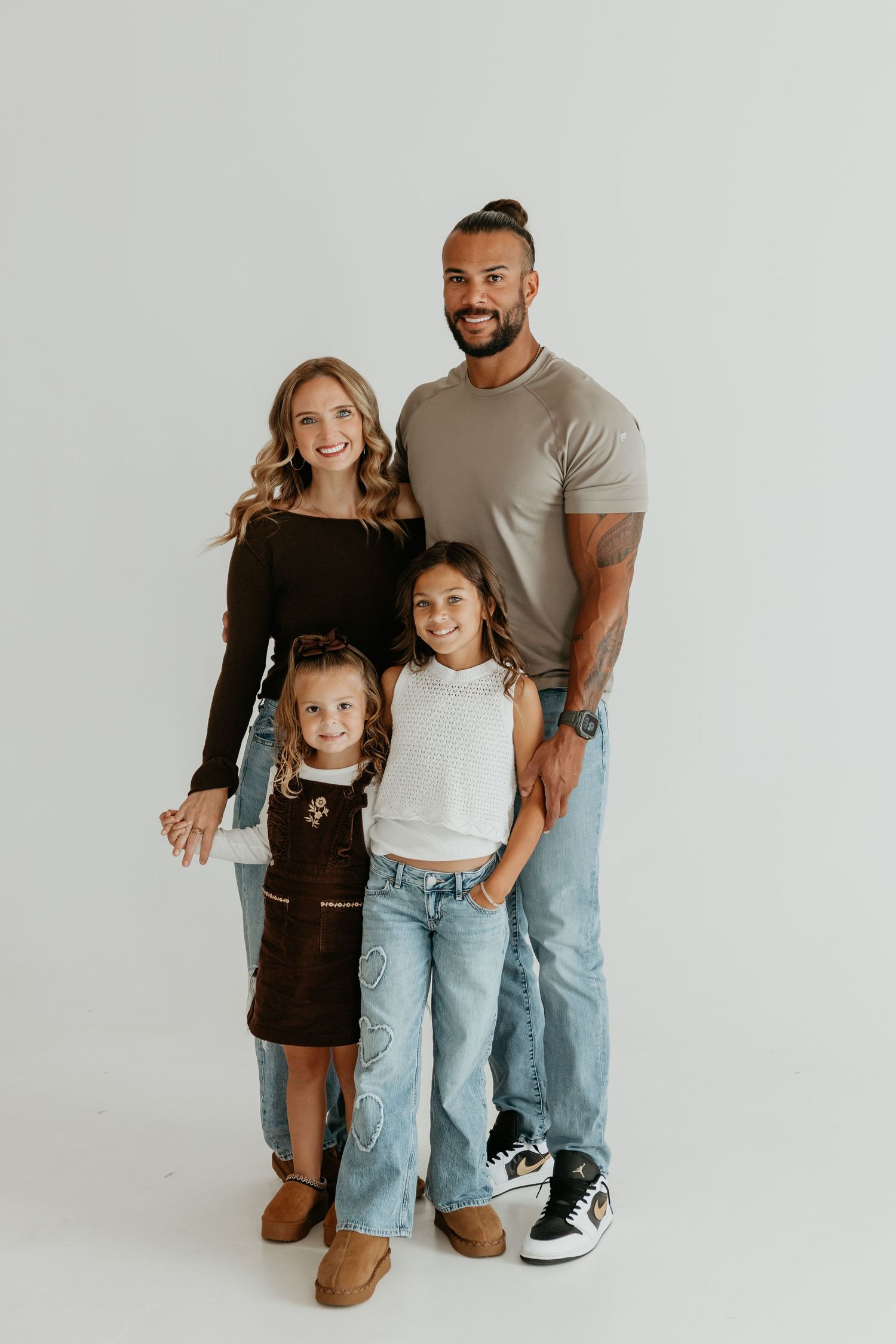 Stylish family standing together against white backdrop in coordinated outfits.