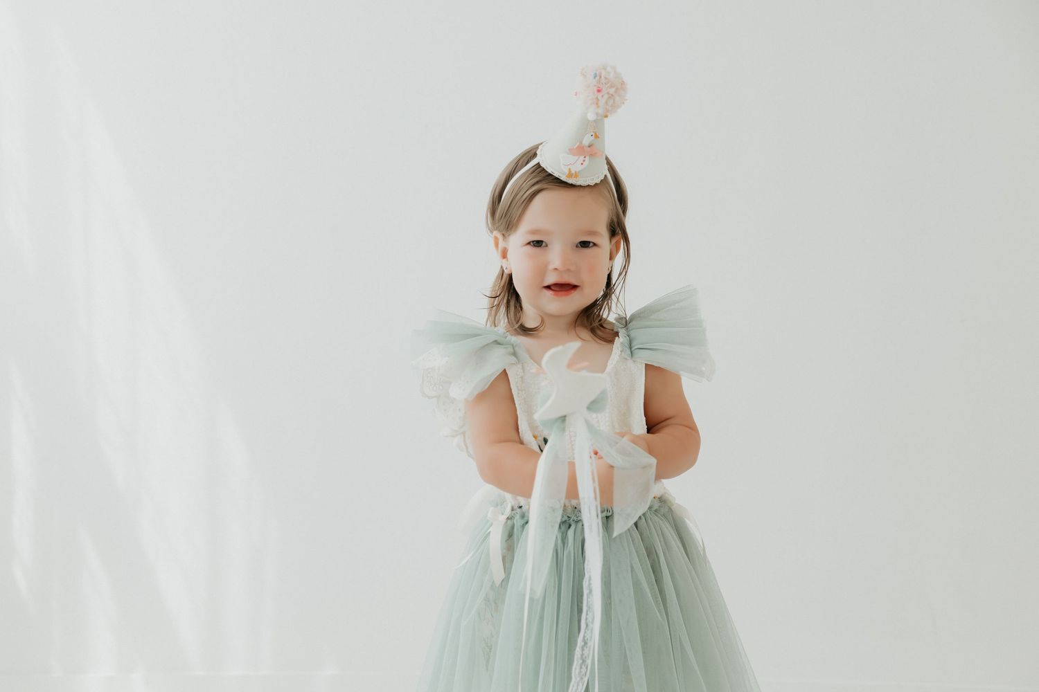 Toddler wearing mint green princess dress twirling in front of white backdrop.