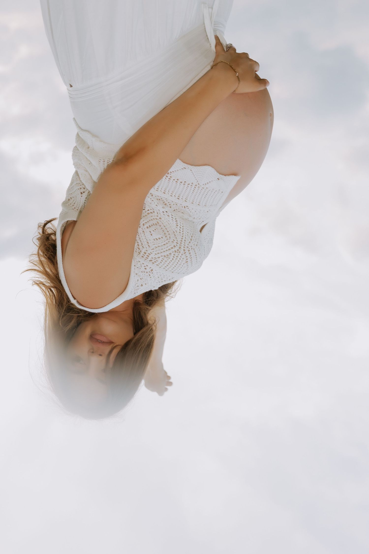An artistic overhead maternity portrait featuring white lace against a cloudy sky.