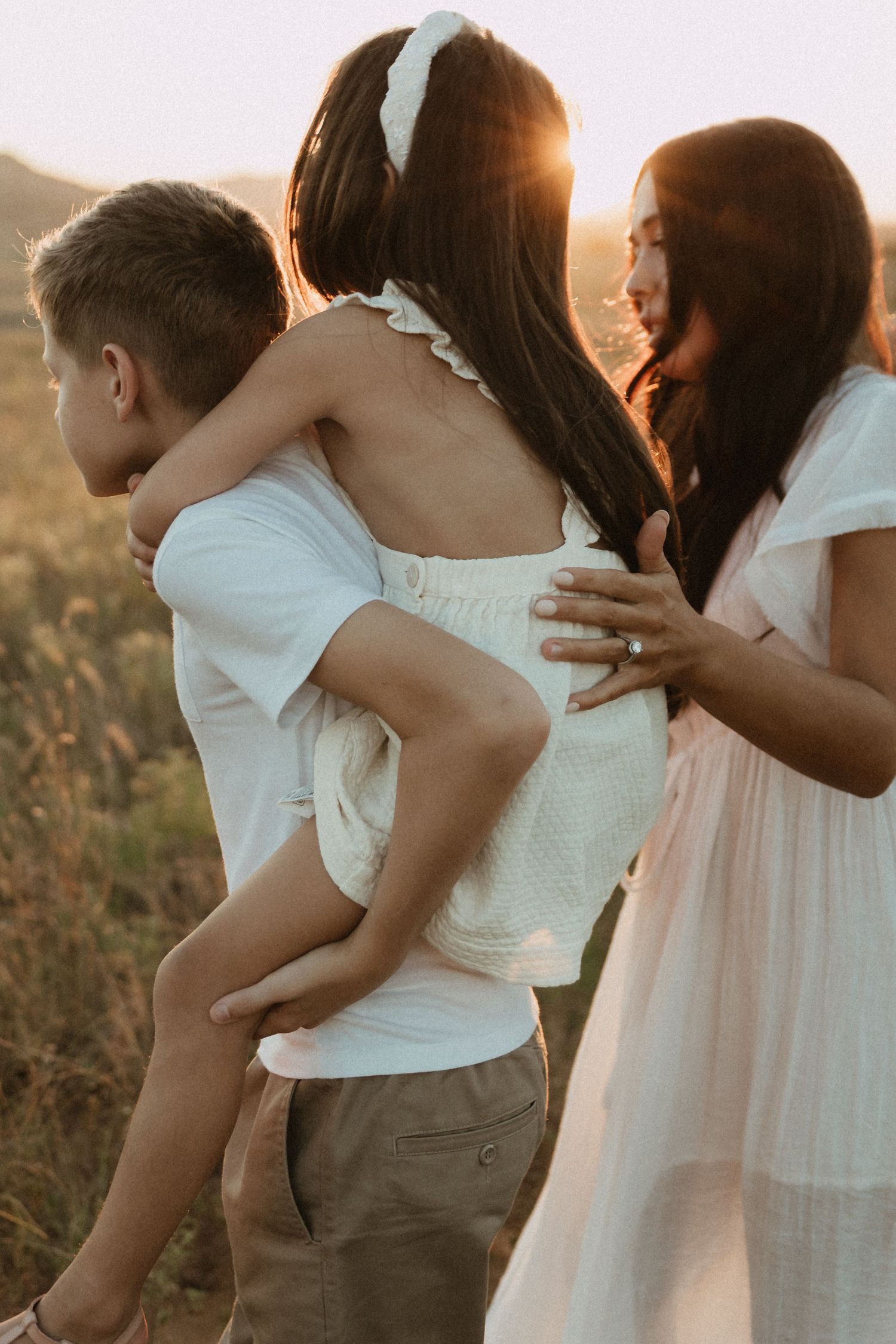 A group embraces in white dresses against a sunset-lit field.