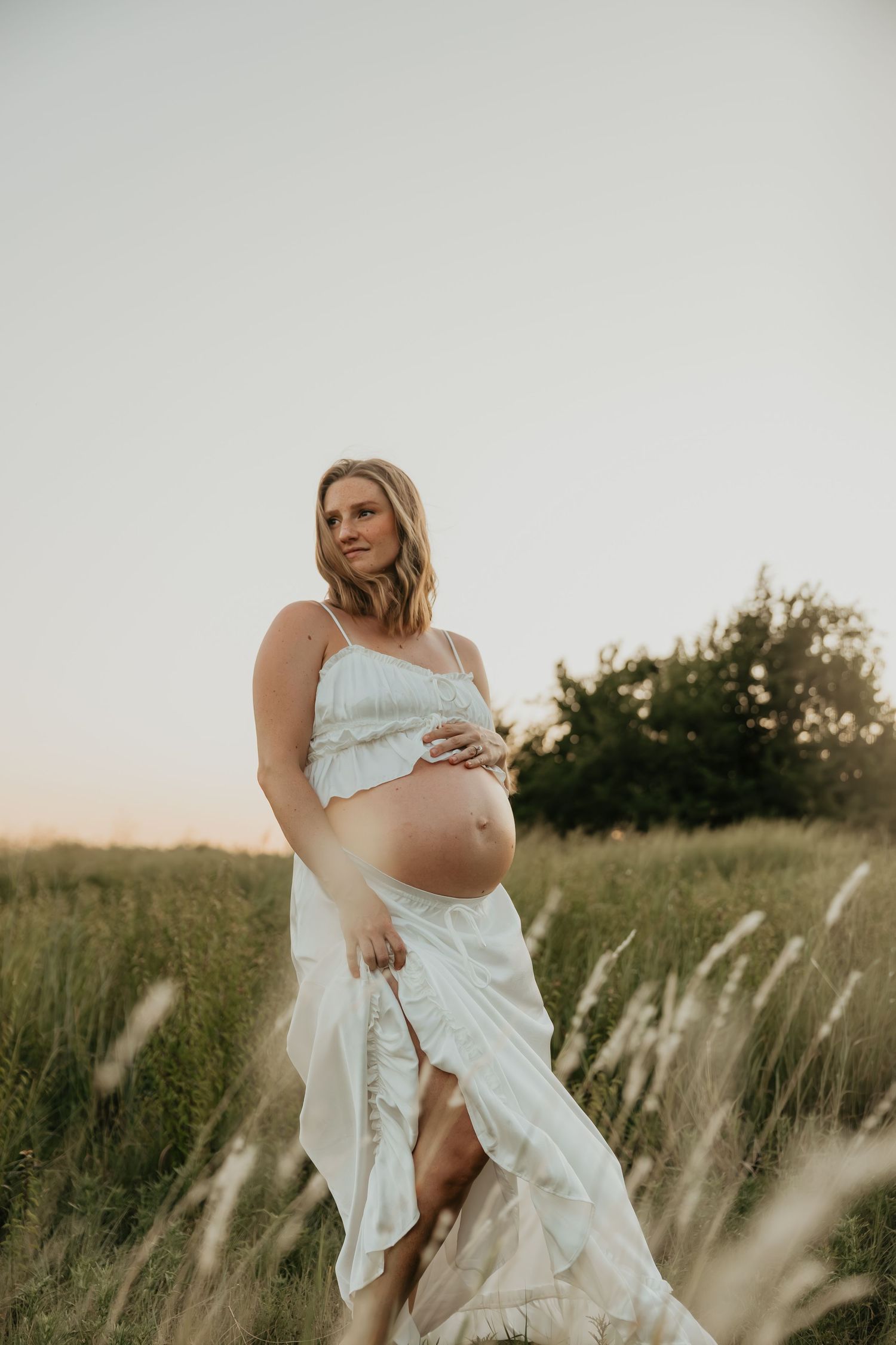 A maternity photoshoot in a field with flowing white dress and natural light.