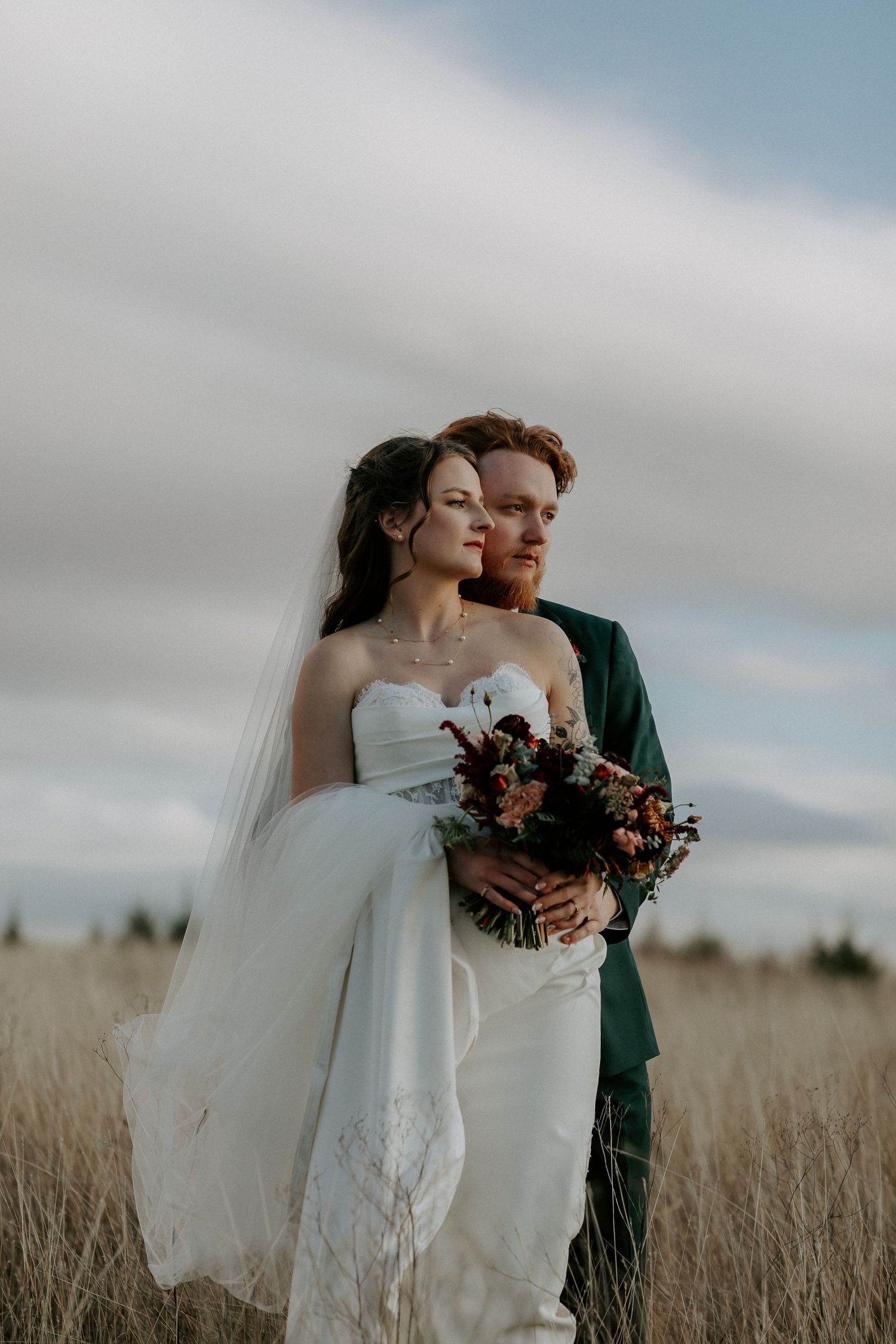 Artistic wedding portraits in a golden field with flowing white dress and dramatic sky.