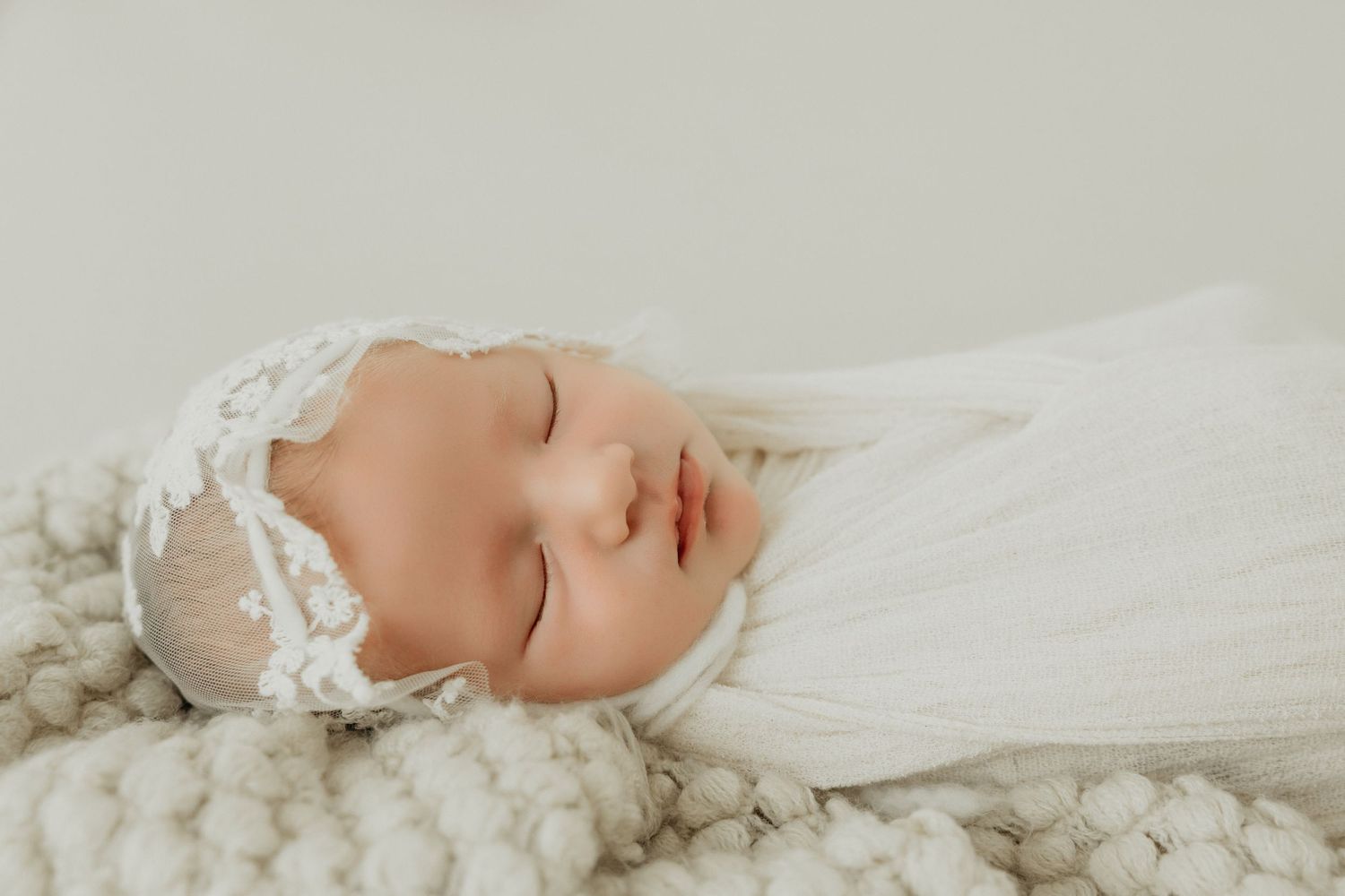 Sleeping newborn on textured white blanket in soft natural light.