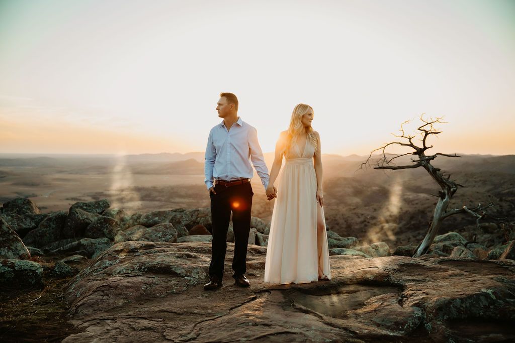 A couple stands on a rocky overlook at sunset wearing formal attire.