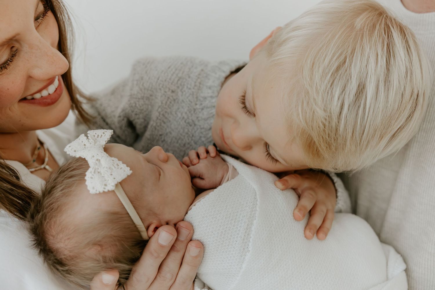 Intimate family portrait showing gentle affection in muted tones against light background.