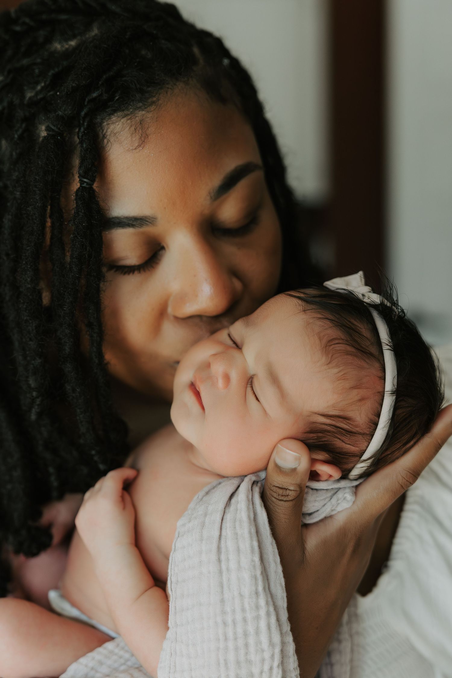 Tender moment with newborn wrapped in white muslin fabric.