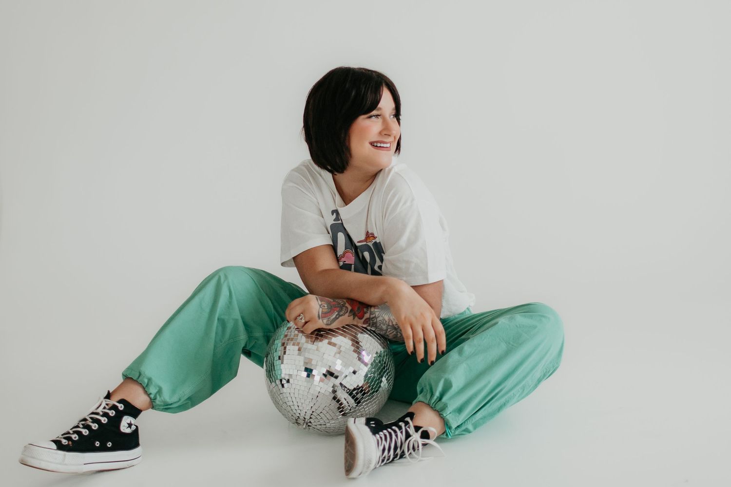 Casual pose with disco ball wearing green pants and graphic tee in studio setting.