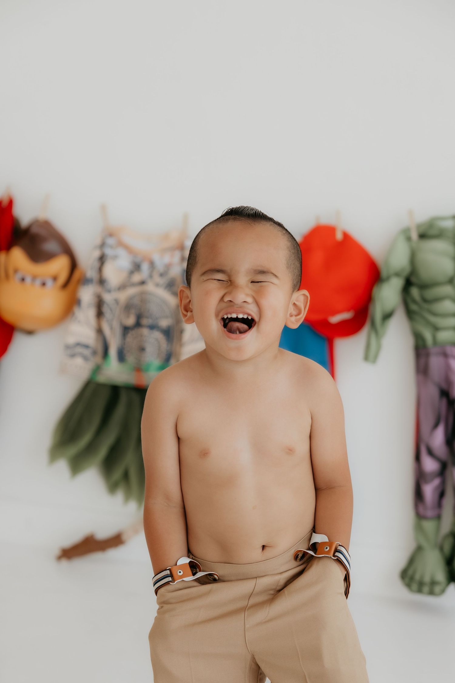 Laughing baby against white wall with colorful plush toys in background.