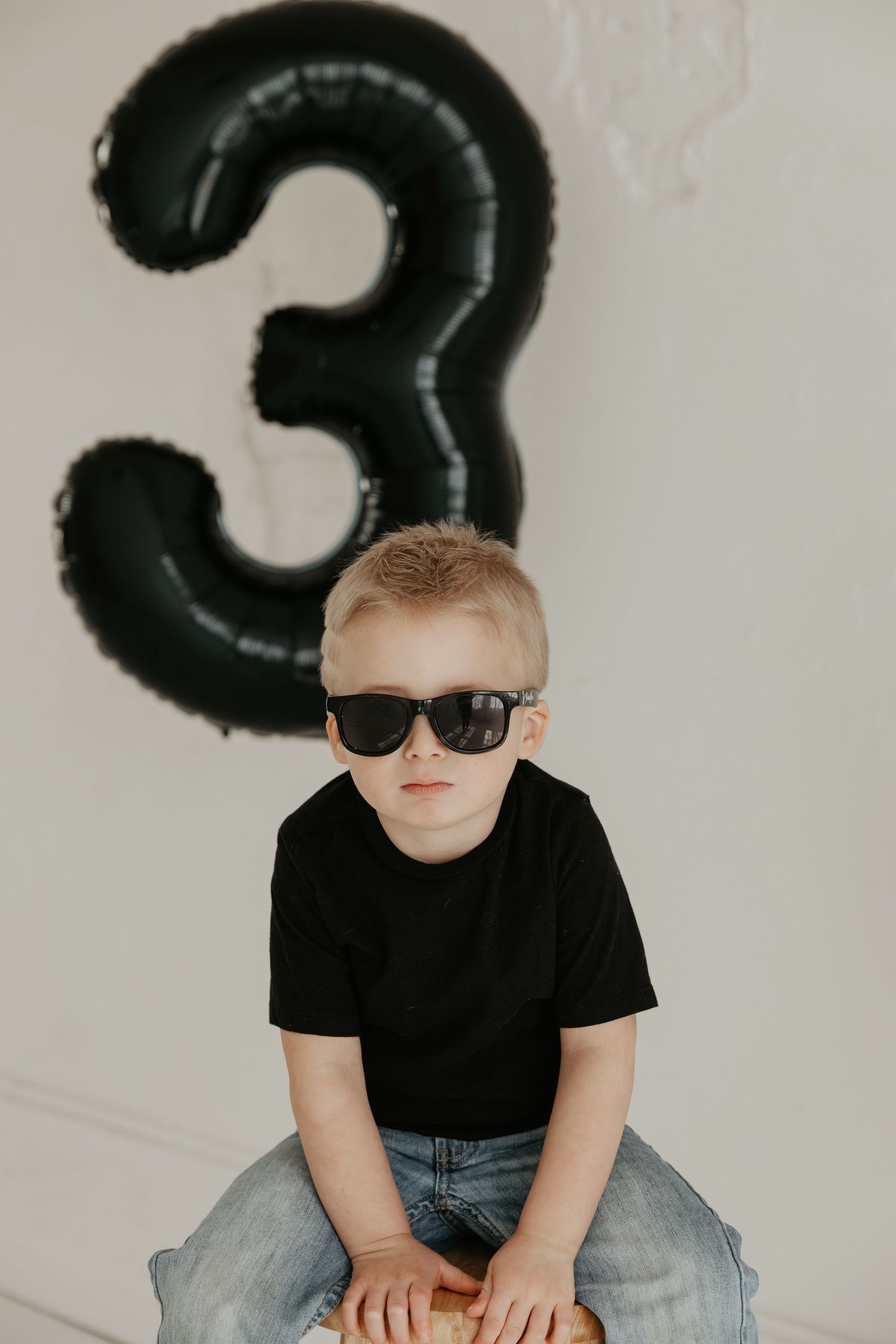 Cool kid in sunglasses and black t-shirt posing with number 3 balloon.
