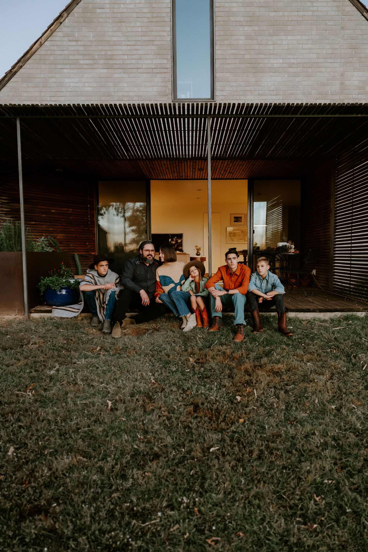 Group relaxing on grass outside modern building with wooden siding.