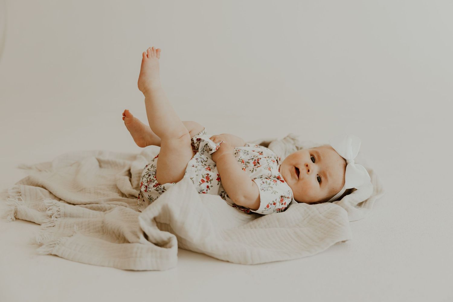 Baby in floral outfit lying on soft white bedding.