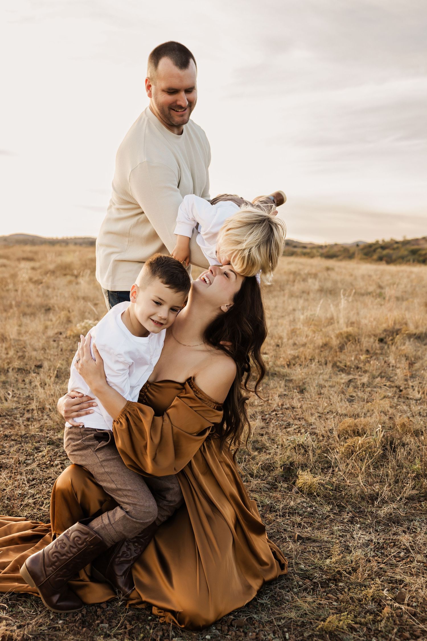 A joyful family moment captured in a brown field during sunset.