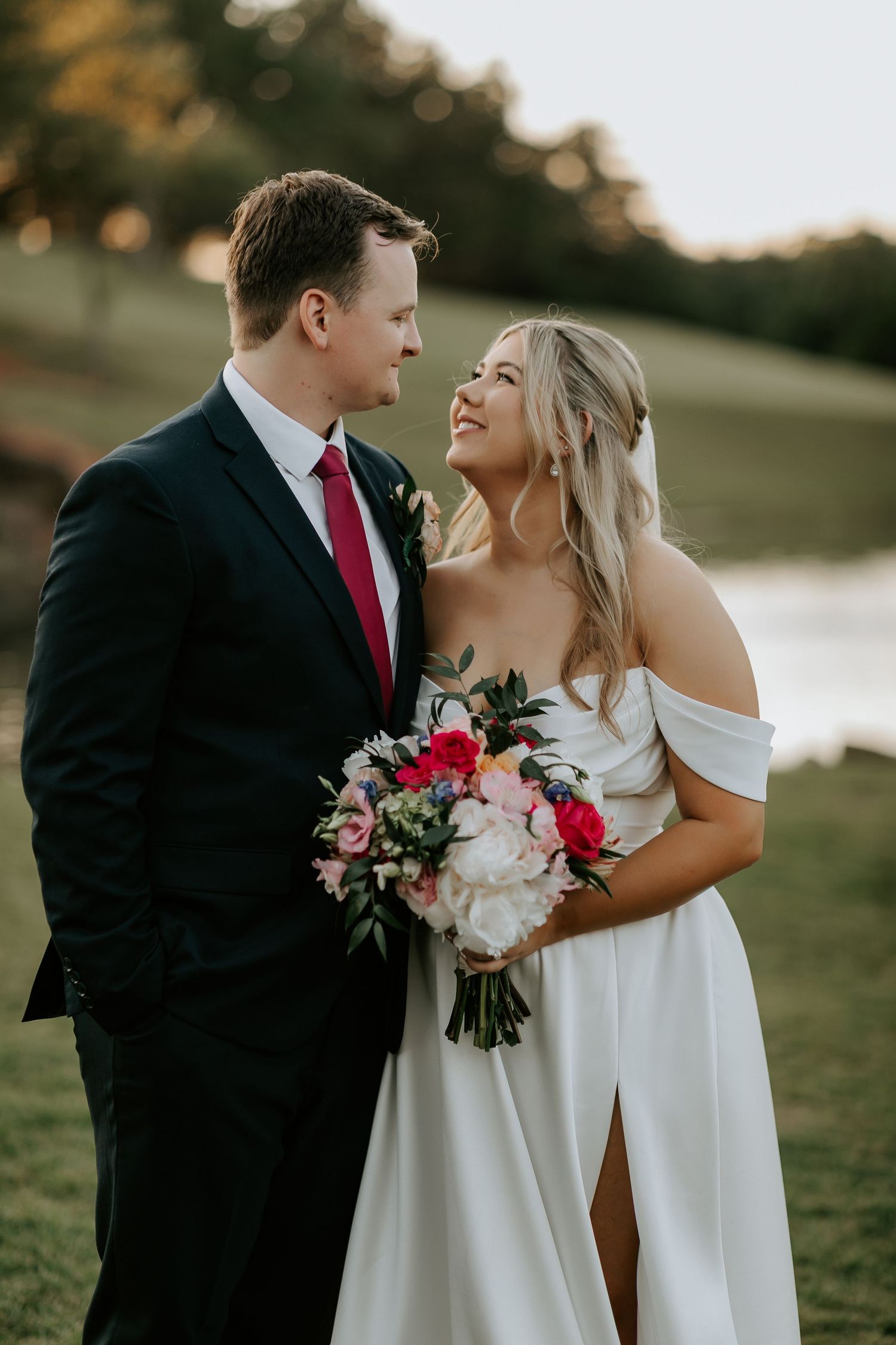 Wedding couple shares joyful moments in an outdoor setting with red and white floral bouquet.