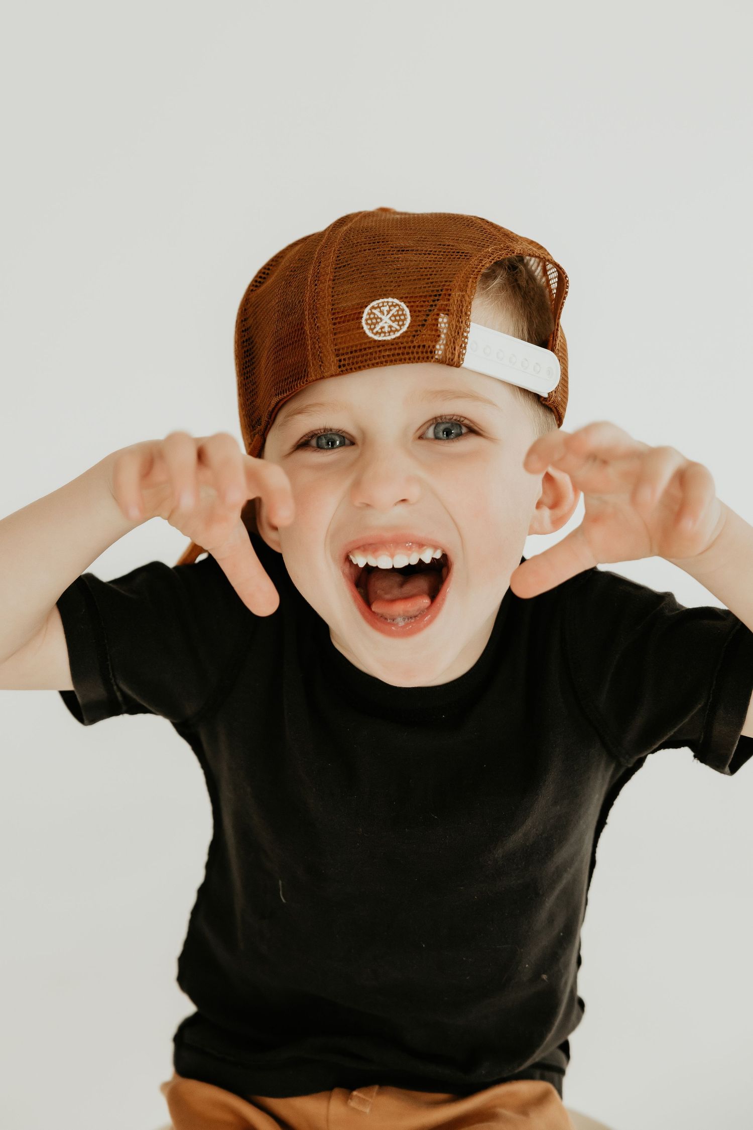 Playful child in black t-shirt and brown baseball cap making silly face against white background.