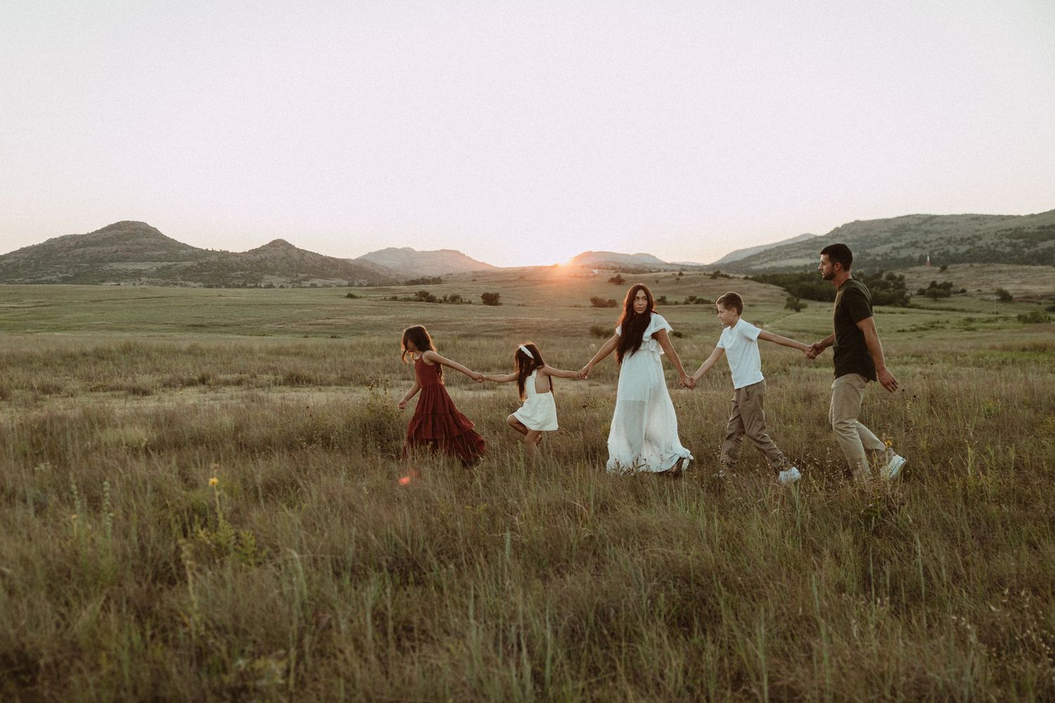 A panoramic view of people walking through a golden field with mountains in the background.