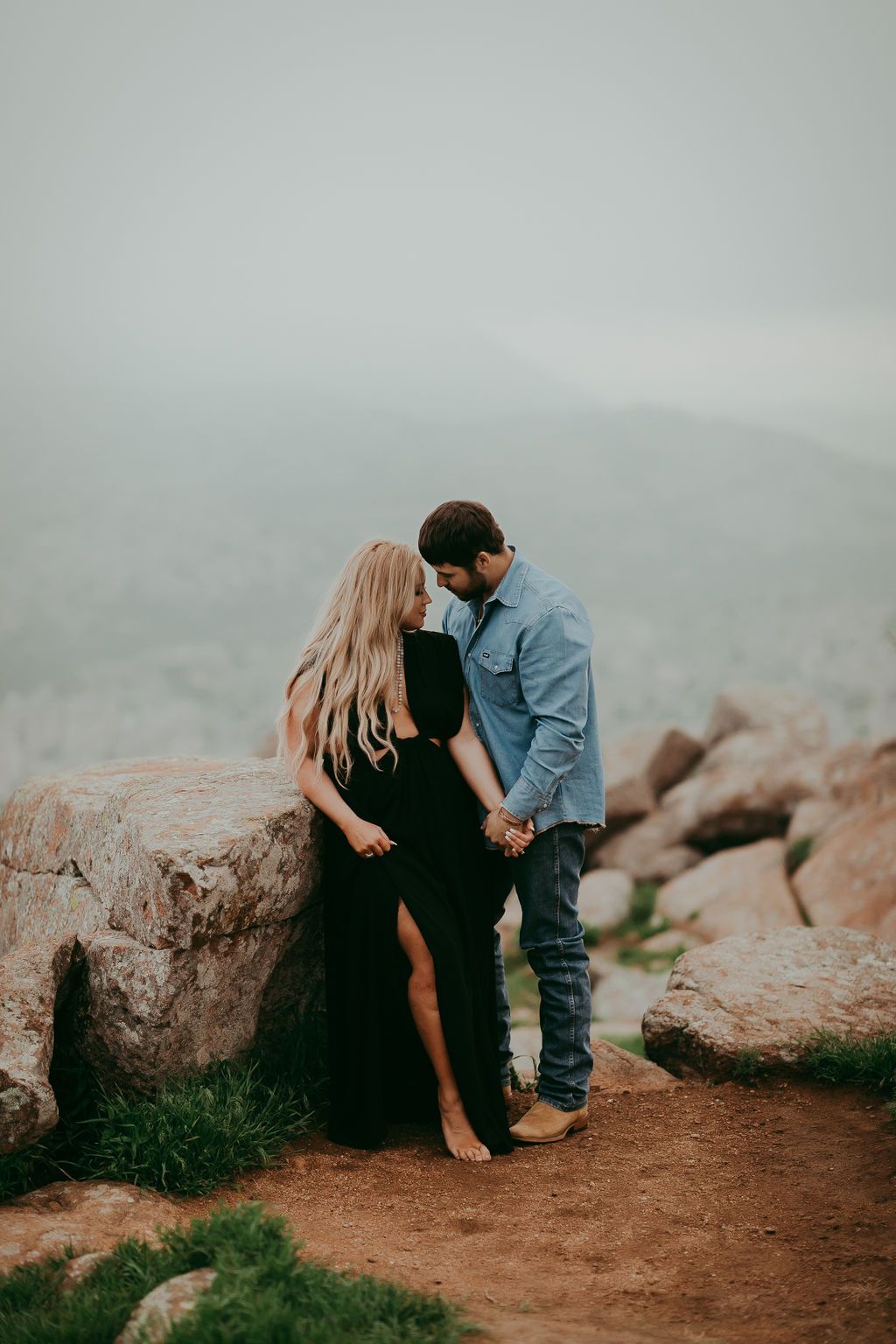 A couple shares an intimate moment on rocky terrain against a misty backdrop.