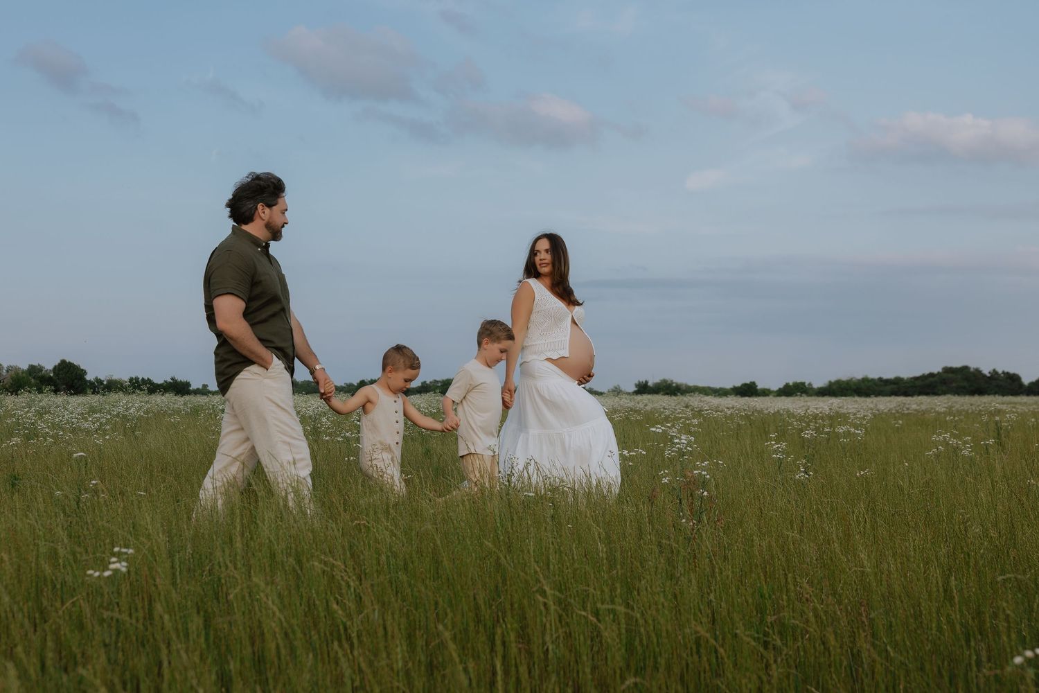 A family walks together through a vast green meadow during sunset.