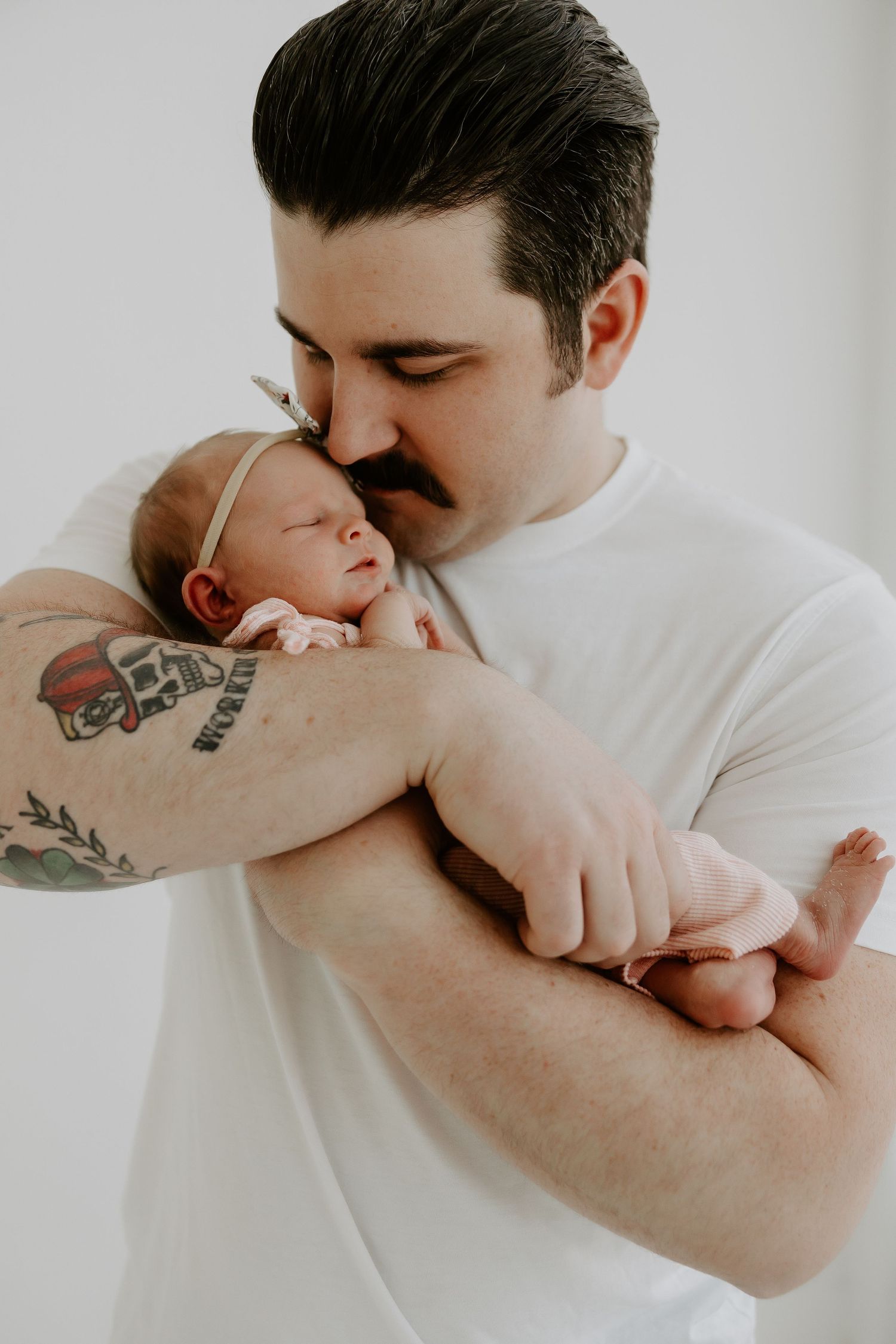 A newborn baby sleeps peacefully in protective arms adorned with tattoos.