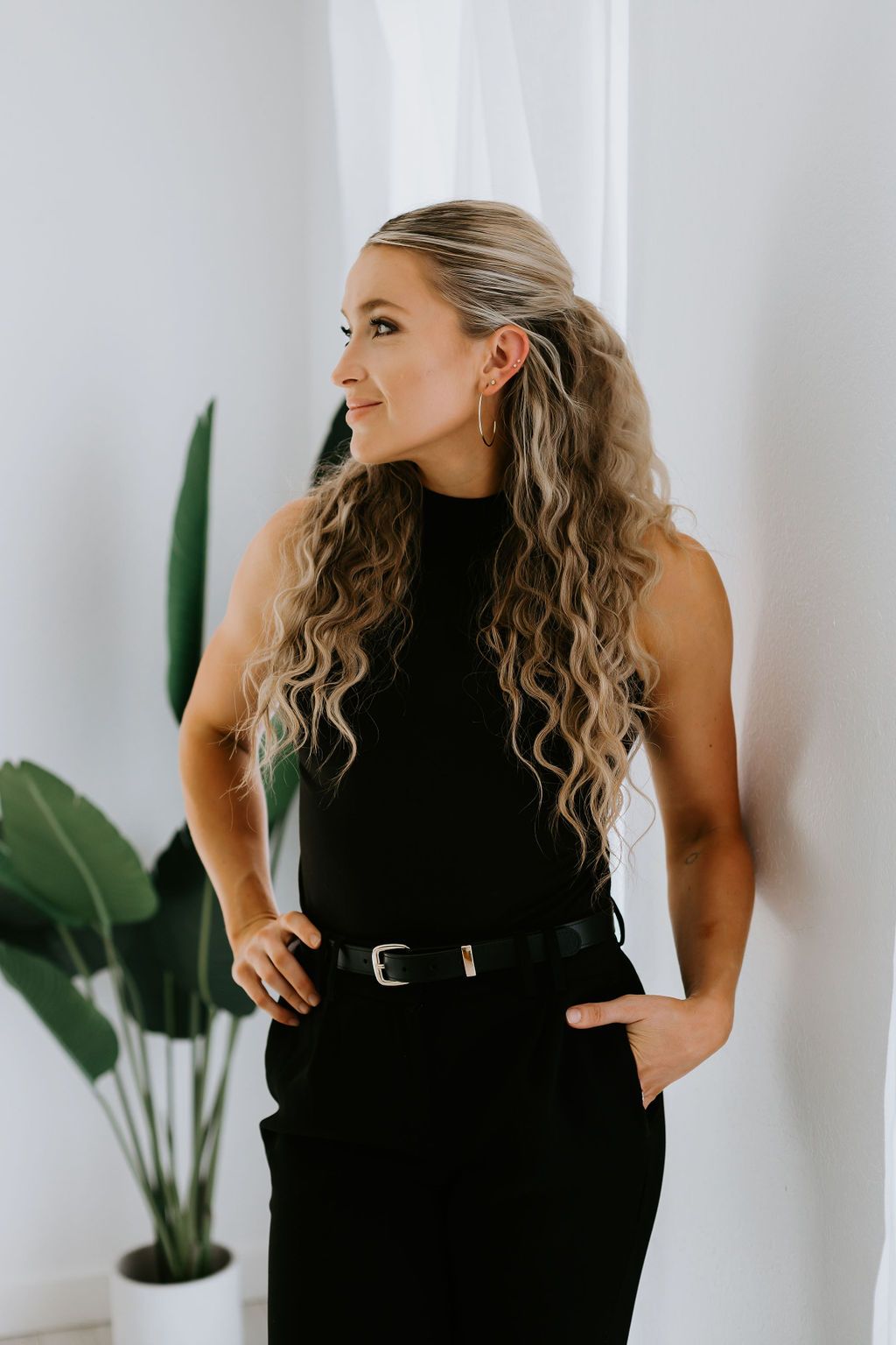 Dynamic poses in black sleeveless outfit against white wall with indoor plants.