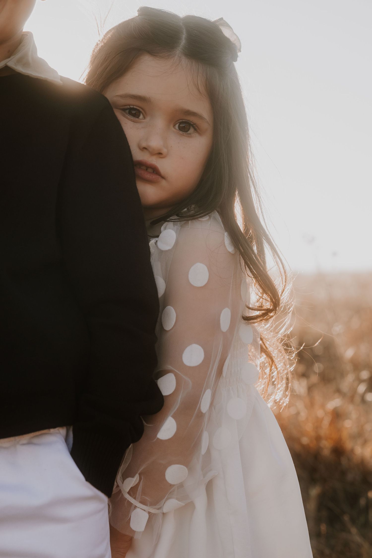 Close-up portrait showing polka dot dress detail in soft golden light.