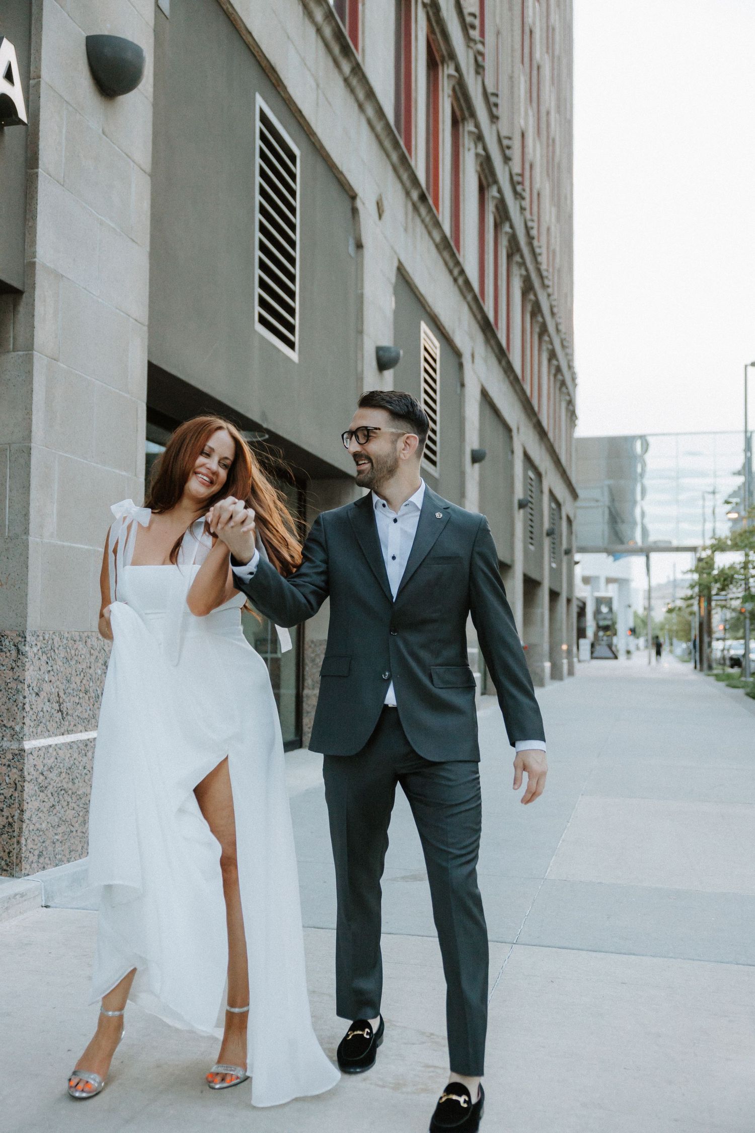 Elegant couple walking and laughing together on urban sidewalk.